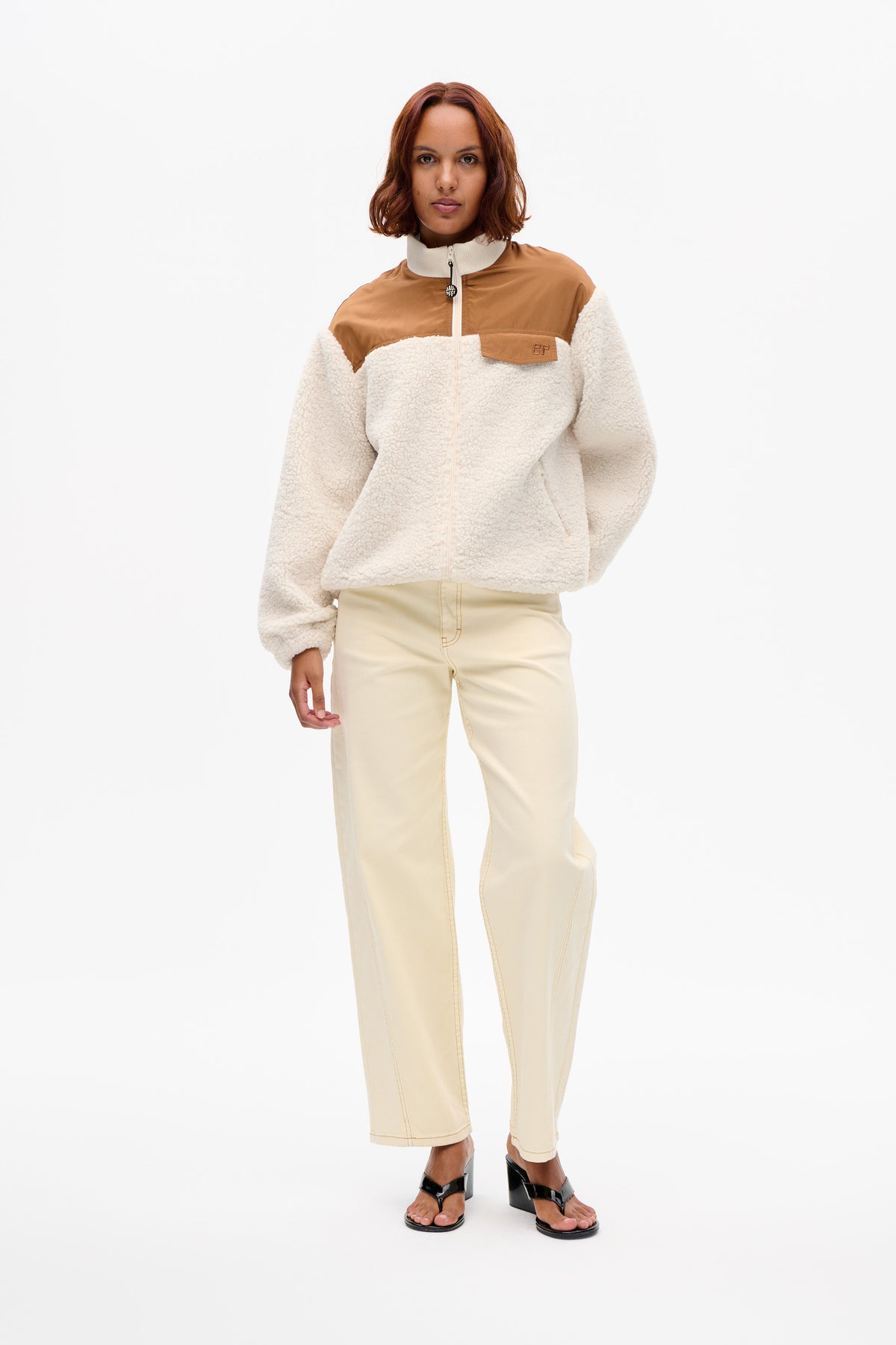Model wearing a cream textured zip-up jacket with tan shoulder panels and a chest pocket, shown from the front.