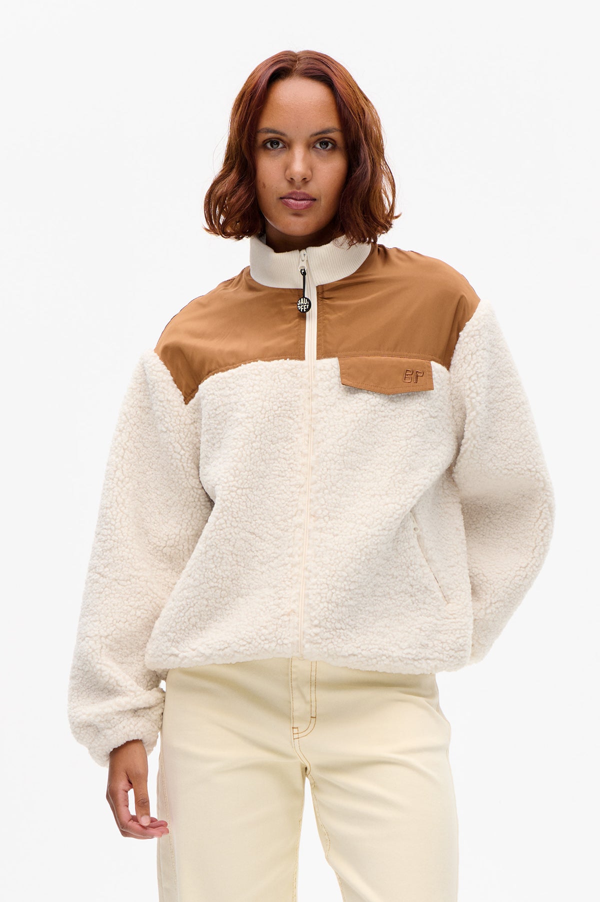 Front view of a cream textured fleece jacket with a tan chest panel, white zip and high ribbed collar, plus a flap pocket.