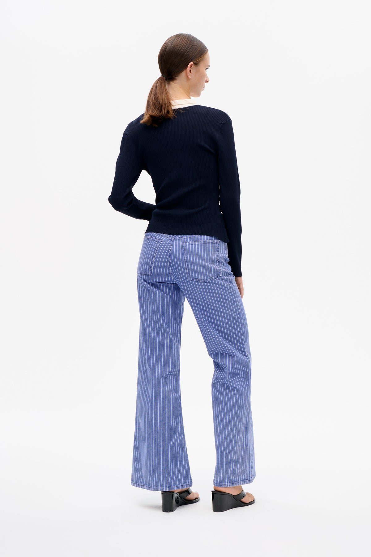 Back view of a model wearing a navy ribbed long-sleeve top with a white collar and blue trousers with fine white pinstripes.
