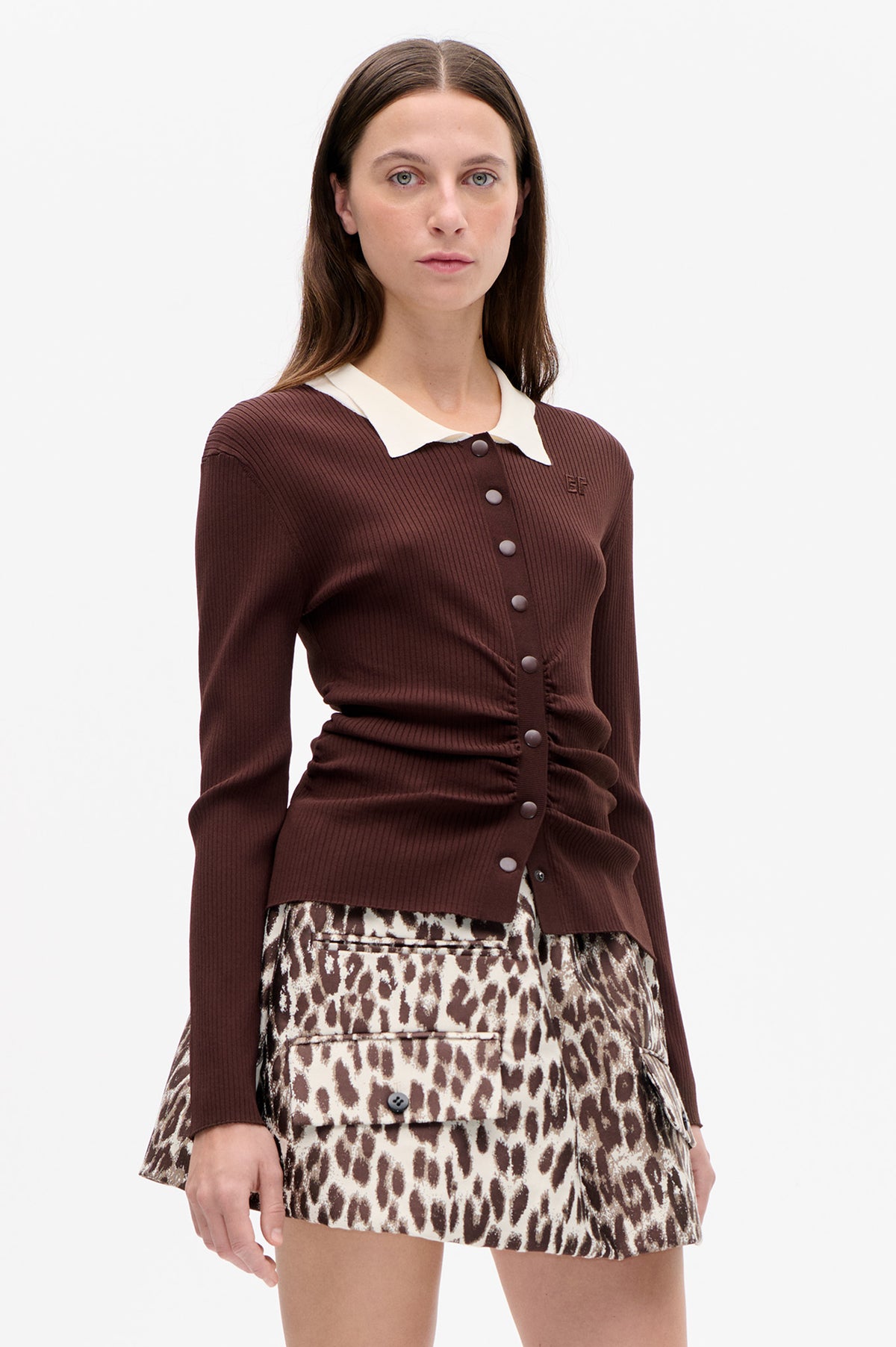 Front detail of a model wearing a dark brown ribbed cardigan with a cream collar and buttons, paired with a brown-and-cream patterned mini skirt.