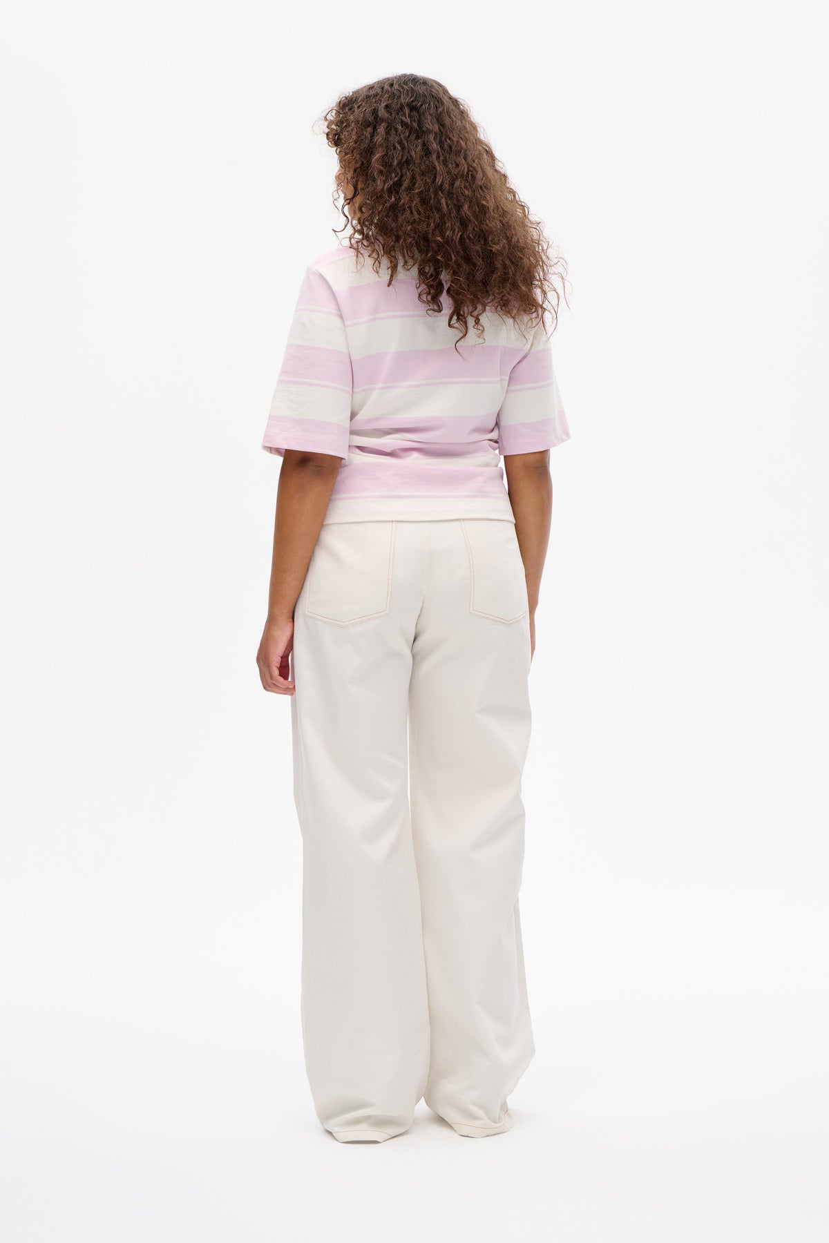 Back view of a model wearing a pink and cream striped short-sleeve T-shirt with cream wide-leg trousers.