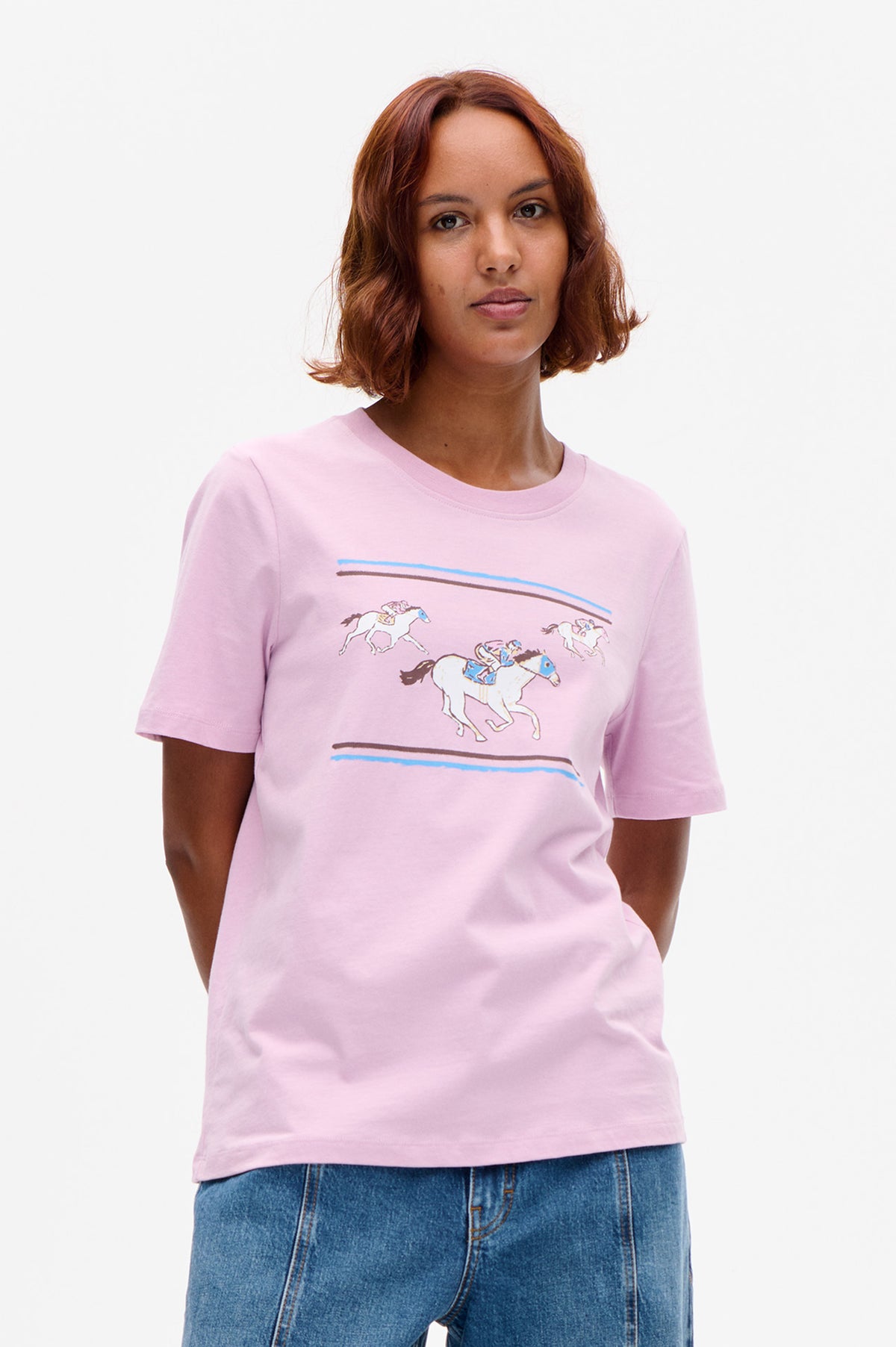 Front view of a light pink short-sleeve T-shirt with a graphic of horses racing between blue and brown lines
