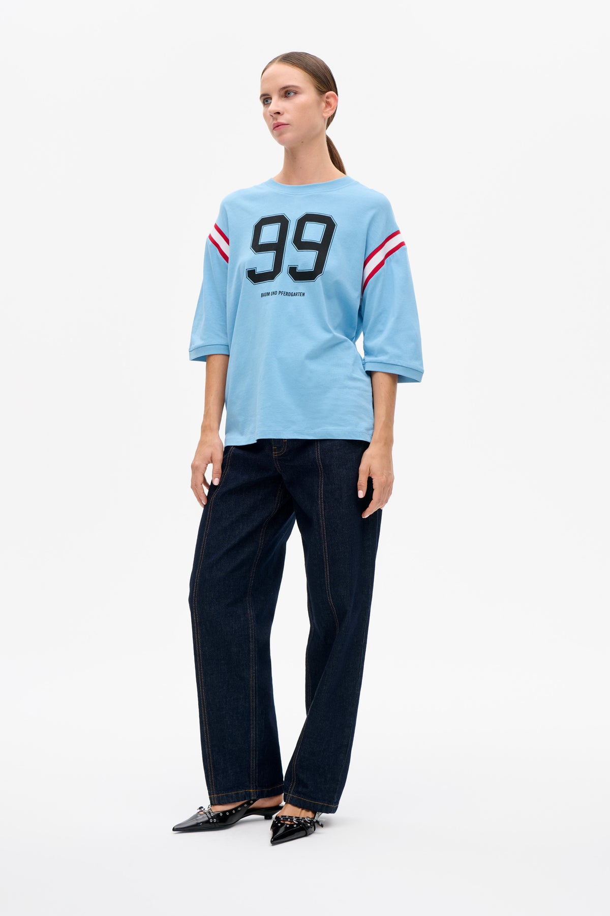 Vorderansicht eines hellblauen oversized T-Shirts mit roten Ärmelstreifen und großem, schwarz umrandetem 99-Motiv.