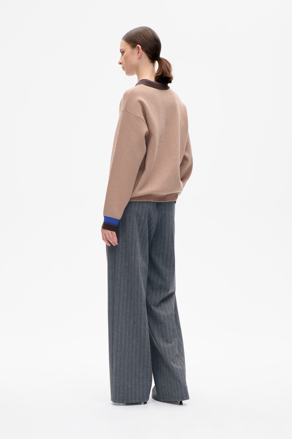 Model shown from the side and back in a taupe sweatshirt with brown and blue ribbed trim and charcoal pinstripe trousers.