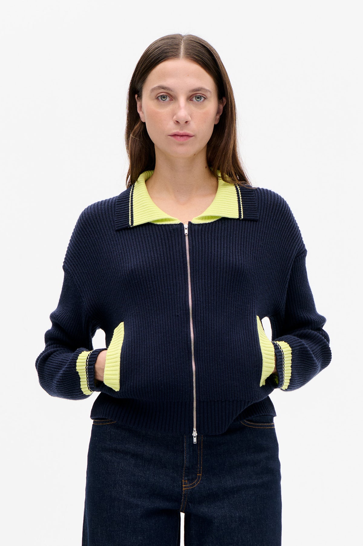 Front view of a model wearing a navy ribbed zip-up cardigan with a lime-green collar and cuffs and contrasting striped trim.