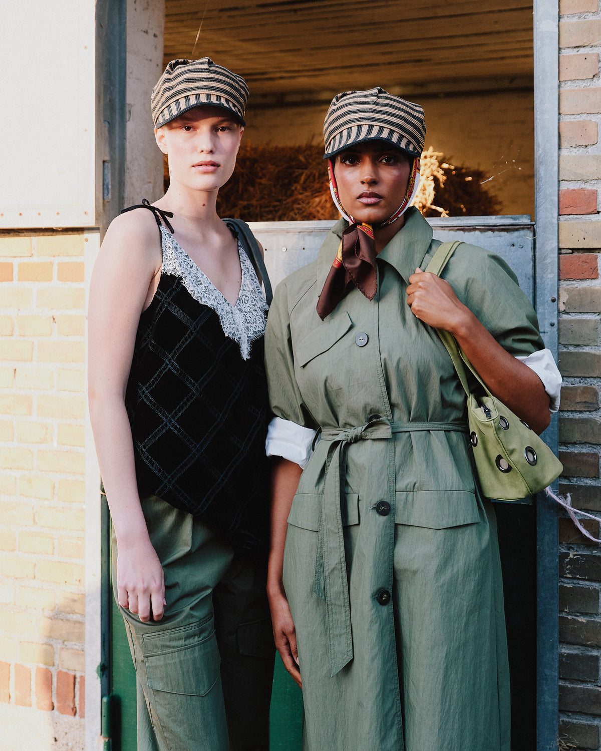 Two models in striped caps: a black lace-trimmed, grid-stitched dress beside a sage belted trench coat and scarf.