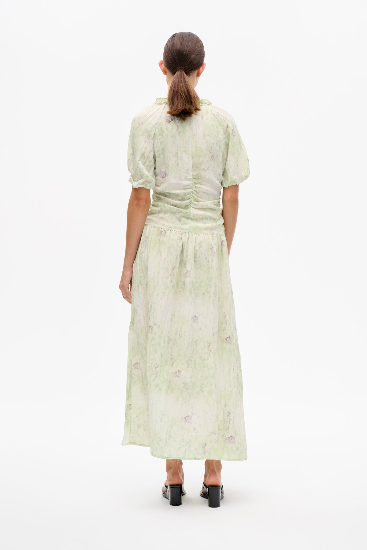 Achteraanzicht van een lichtgroene en crème midi-jurk met bloemenprint, korte pofmouwen, ruches aan de halslijn en een taille met plooien.