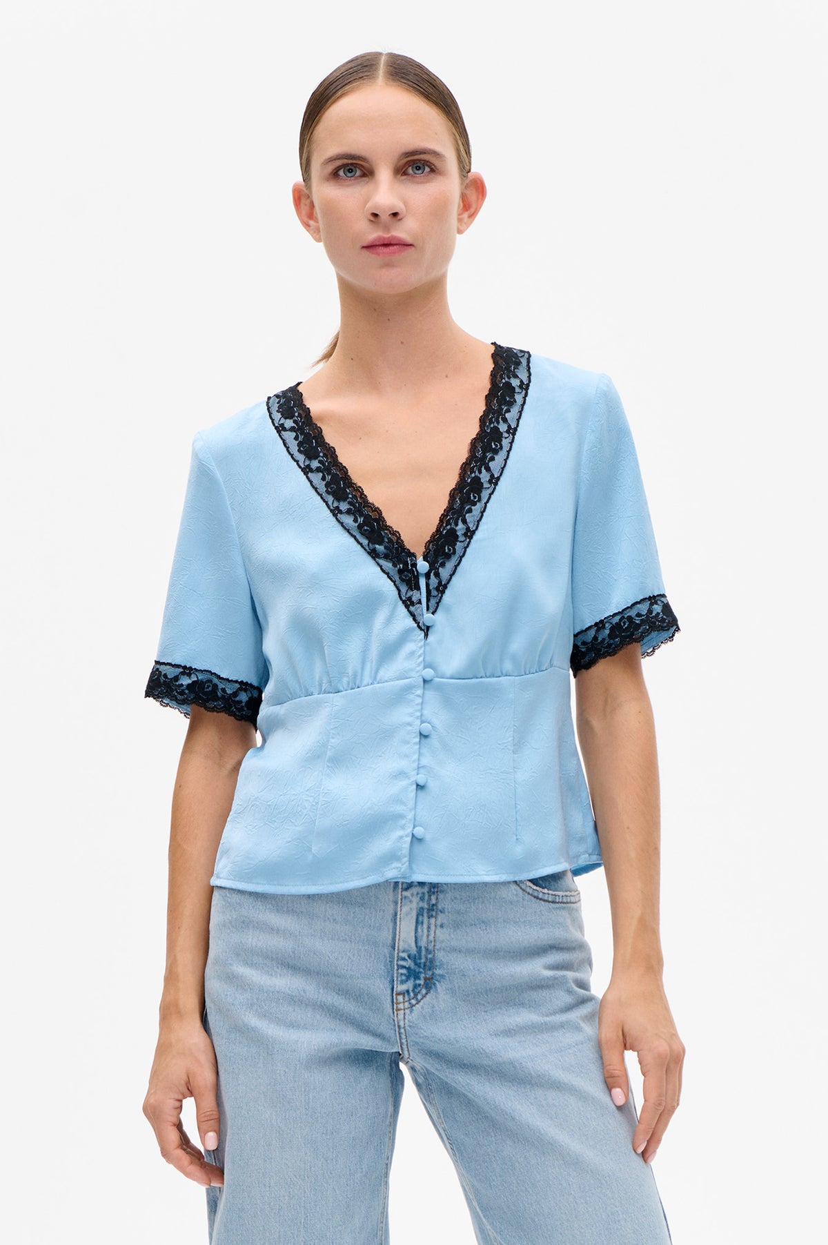 Front view of a pale blue textured short-sleeve blouse with black lace V-neck trim, lace cuffs and covered buttons.