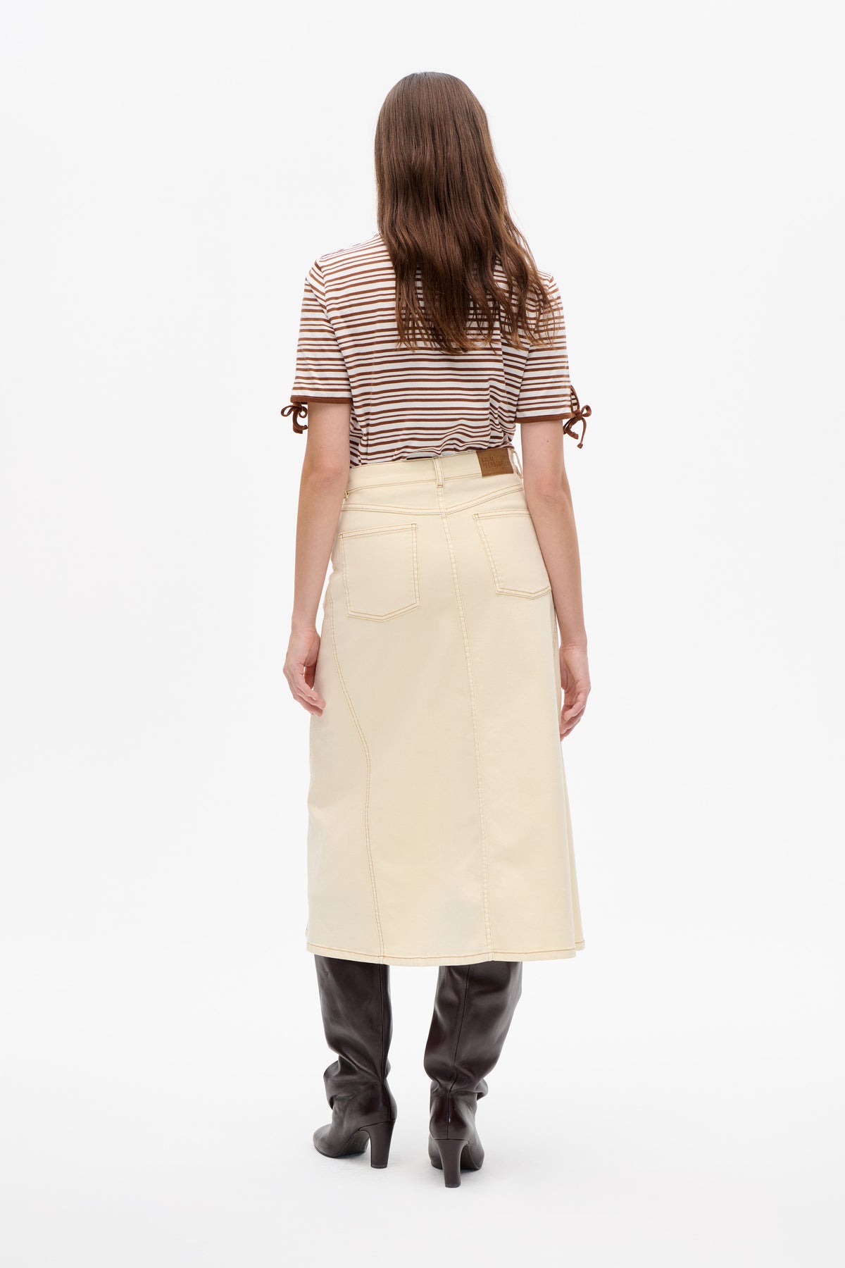 Back view of a model wearing a brown-and-white striped short-sleeve T-shirt with tied sleeve details and a cream denim skirt.