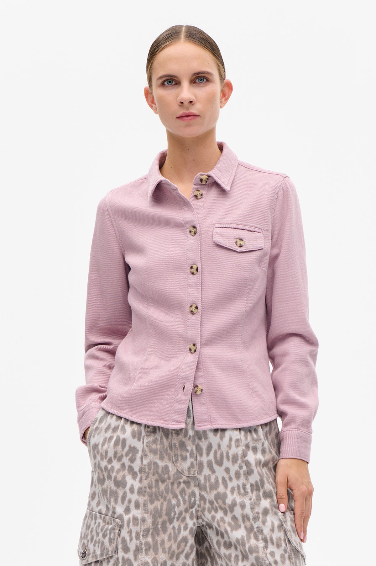 Front view of a model wearing a pale pink button-front jacket with a pointed collar and flap chest pocket, paired with grey animal-print trousers.