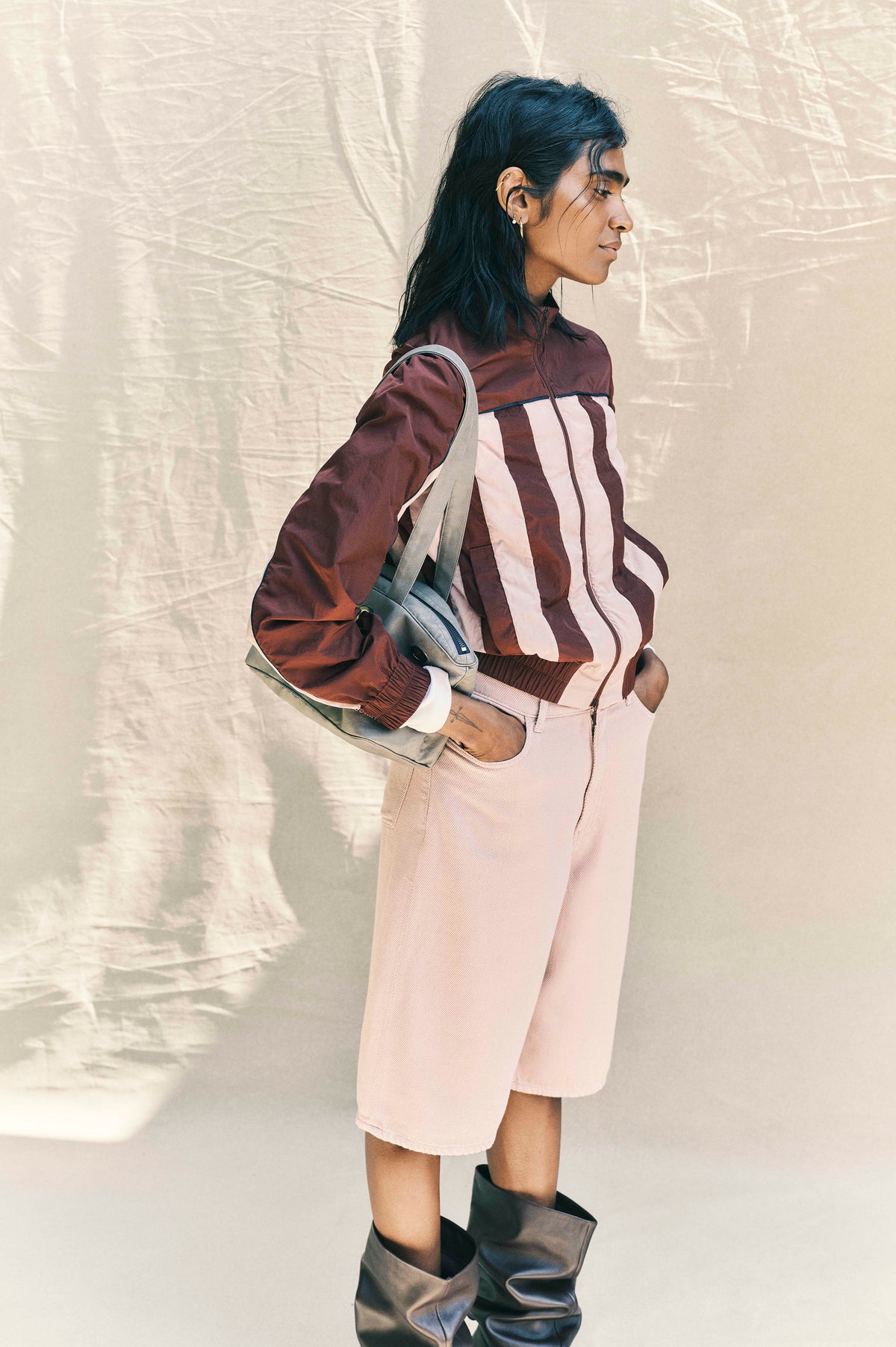 Campaign portrait of a model in a burgundy and pale pink colour-block zip jacket and pale pink shorts, carrying a grey shoulder bag.