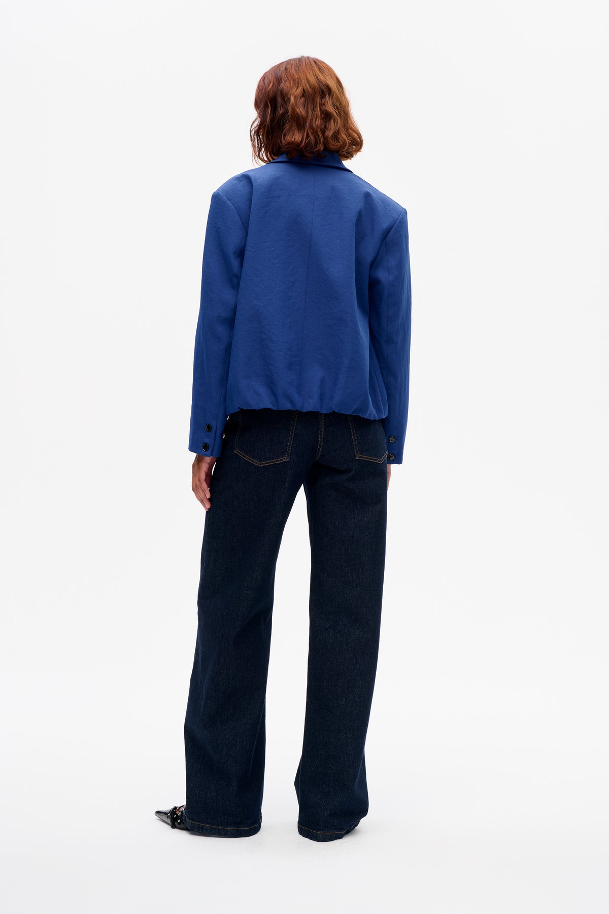 Back view of a model wearing a cobalt blue jacket with a notched collar and buttoned cuffs, paired with dark wide-leg jeans.