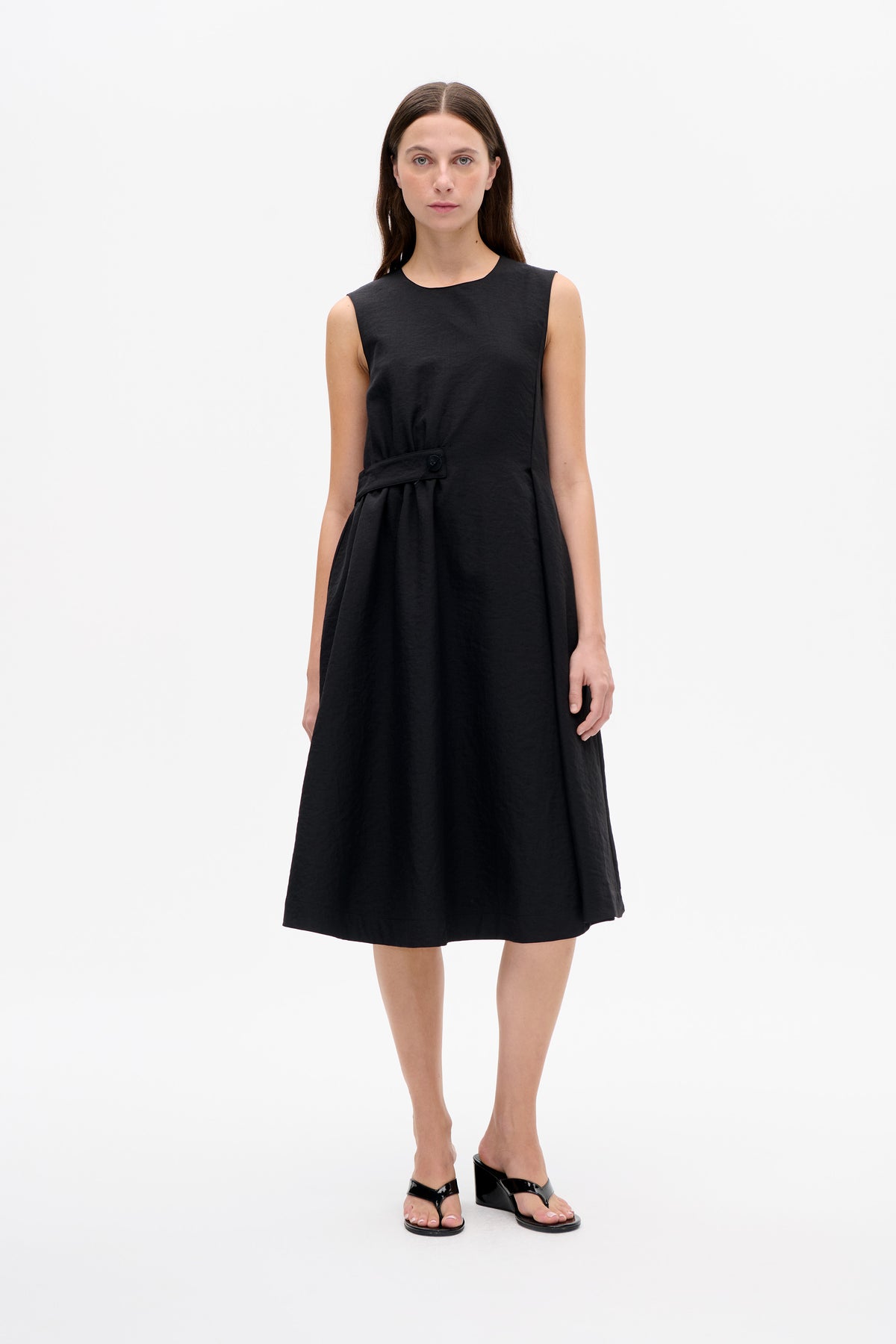 Front view of a black sleeveless A-line dress with a round neckline and gathered waist detail secured by a buckle tab.