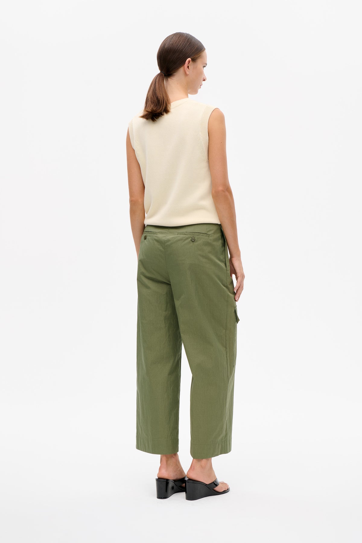 Rear three-quarter view of a model wearing an ivory sleeveless knit top, olive wide-leg cropped trousers and black wedge sandals.
