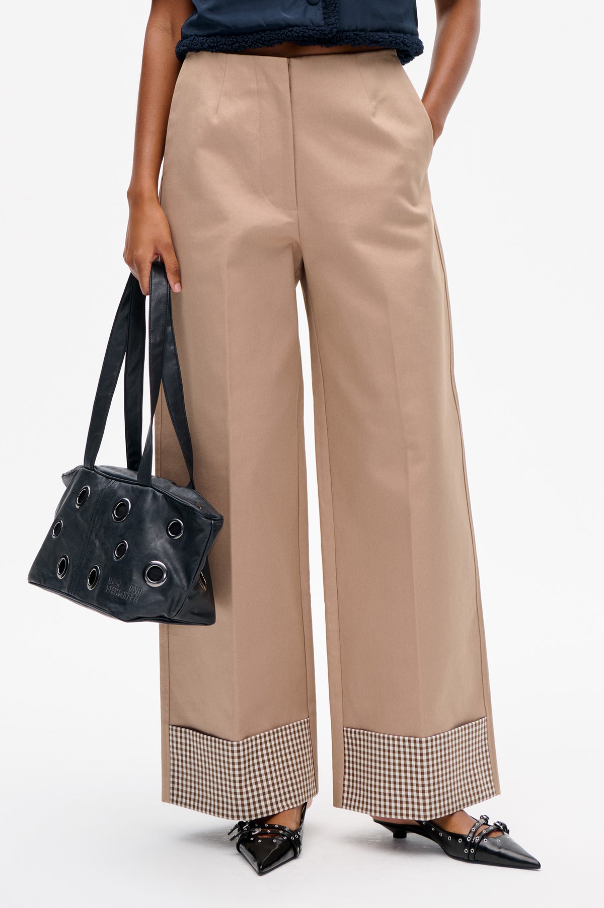 Close-up of beige wide-leg trousers with brown-and-cream gingham cuffs, styled with a navy top and black accessories.