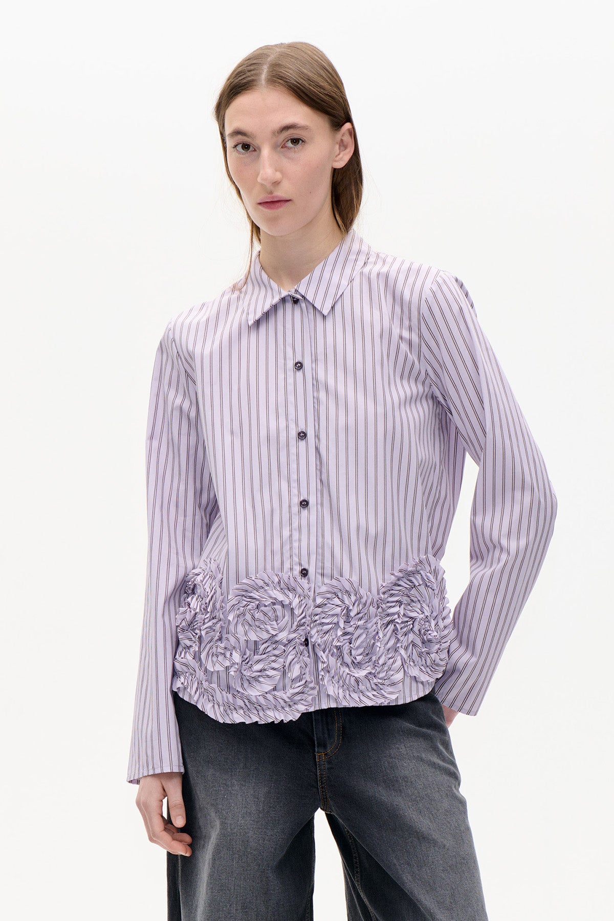 Model wearing a pale lavender striped button-front shirt with long sleeves and sculptural ruffled detailing around the hem.