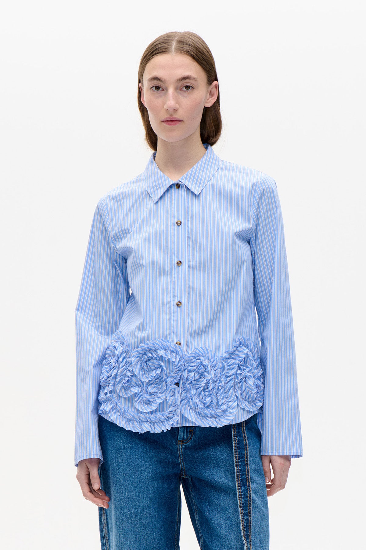 Vooraanzicht van een lichtblauw-wit gestreepte blouse met knoopsluiting aan de voorkant, lange mouwen, een puntige kraag en een gerimpelde volant bij de zoom.