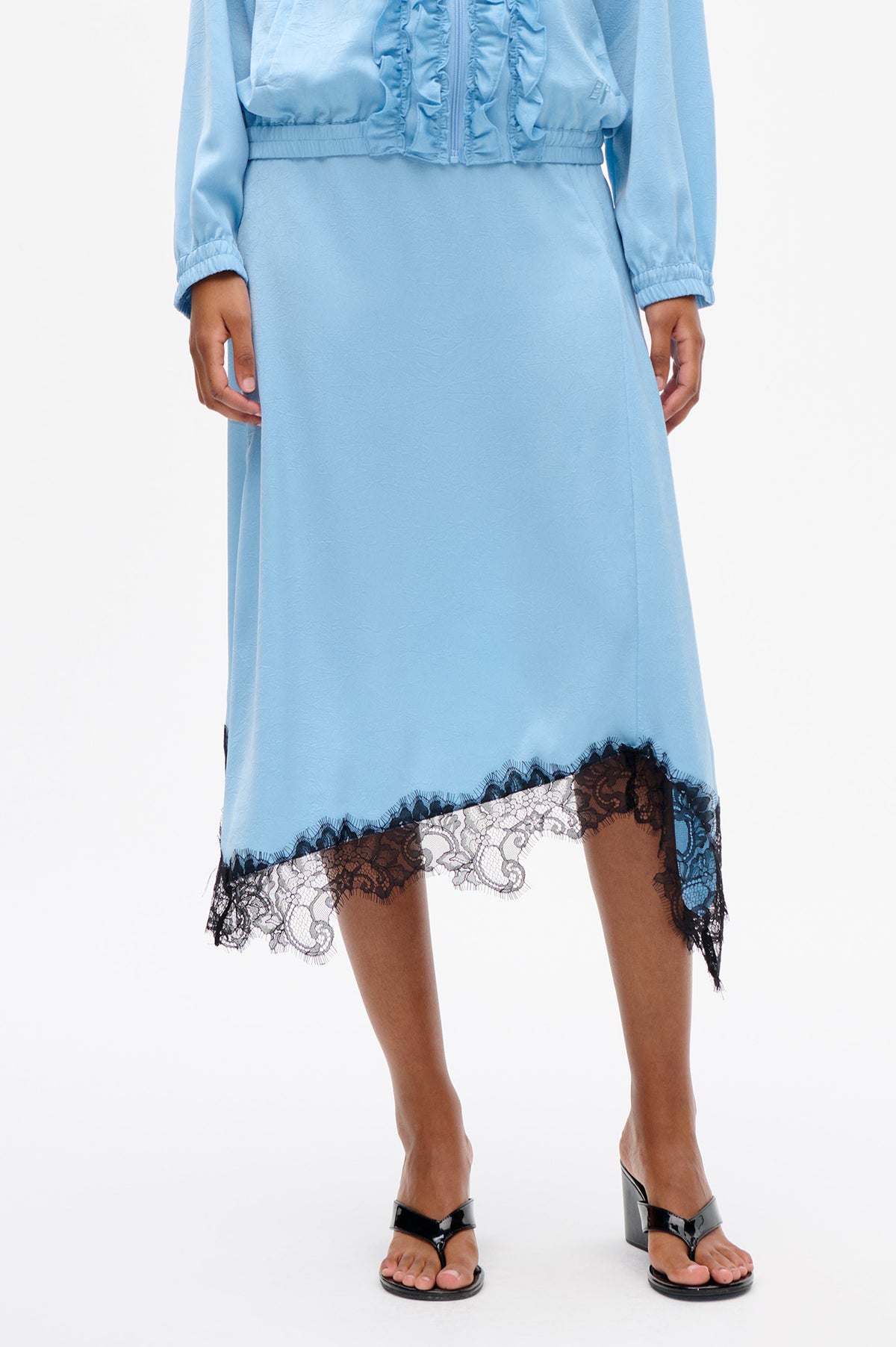 Front detail of a light blue dress with a cropped ruffled zip-front jacket and black-and-cream lace trim at the hem.