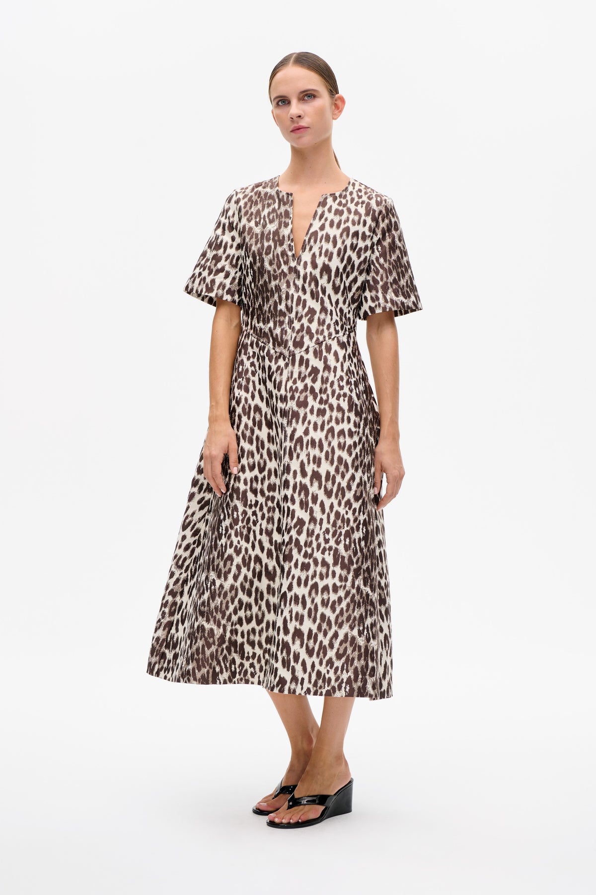 Front view of a model wearing a beige and brown animal-print dress with a split neckline and wide short sleeves.