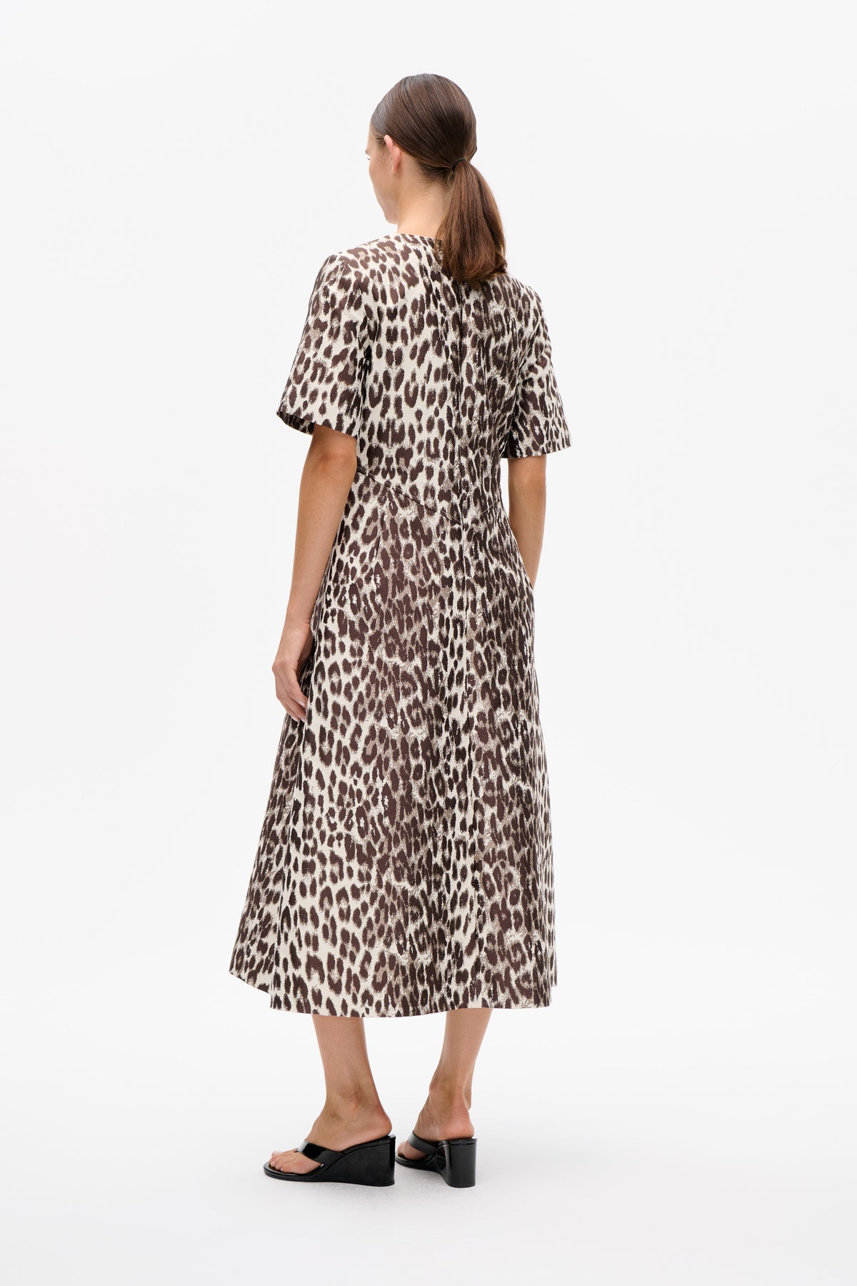 Back view of a model wearing a brown and cream animal-print short-sleeved midi dress with black wedge sandals.