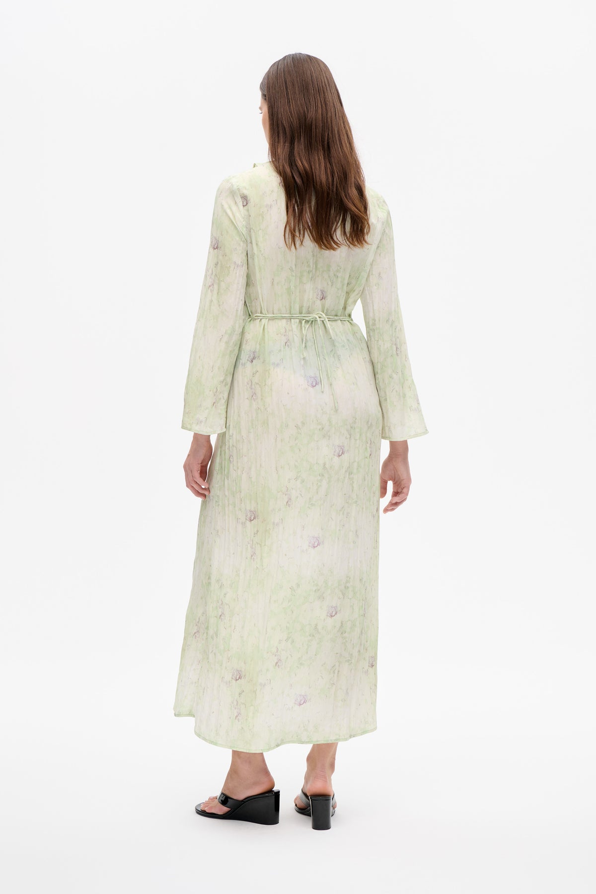 Back view of a long-sleeved, midi-length dress in a pale green and cream abstract floral print, tied at the waist.