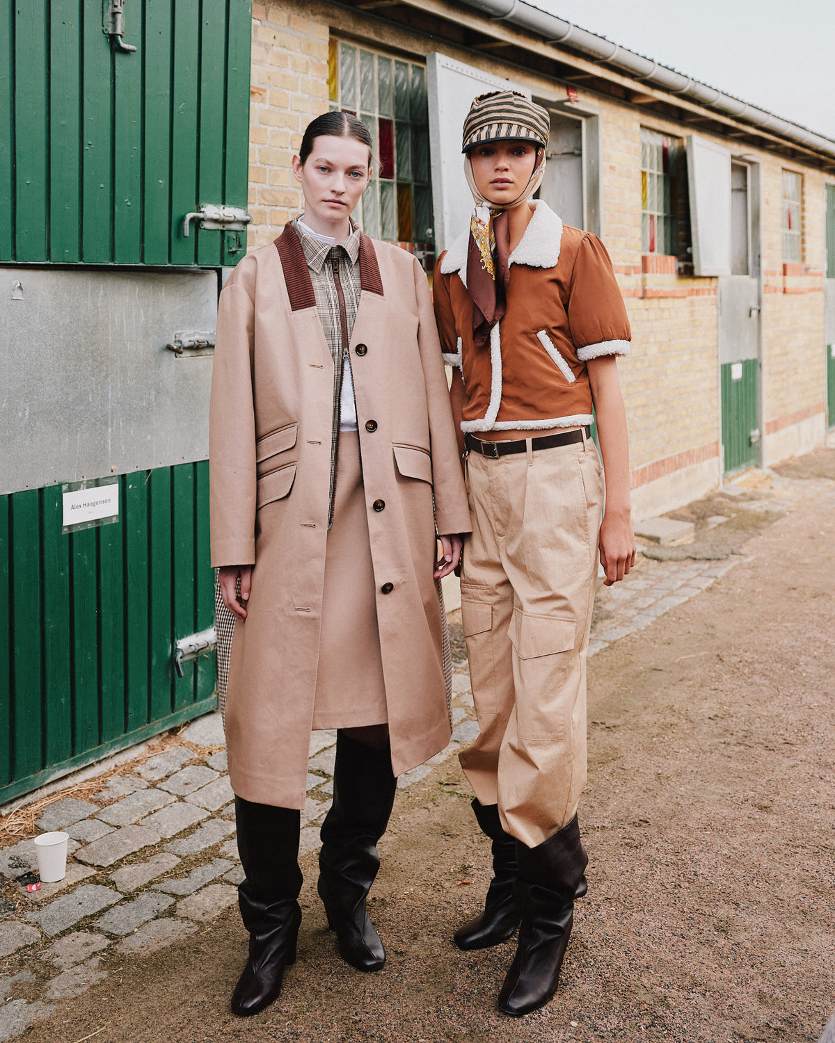 Two models wear a beige long coat and plaid shirt, and a rust shearling-trimmed jacket with beige cargo trousers and a patterned headscarf.