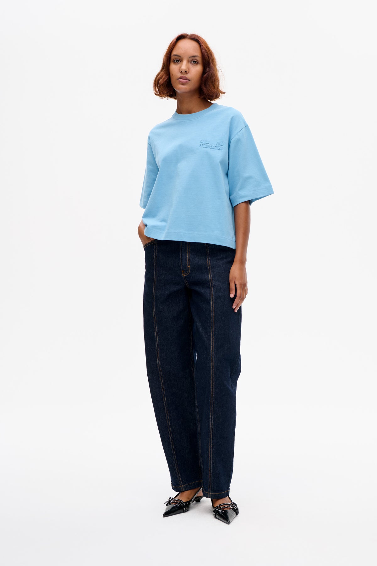 Mannequin portant un T-shirt oversized bleu clair à manches courtes, avec un logo en relief sur la poitrine, et un jean ample à jambes larges de couleur foncée.