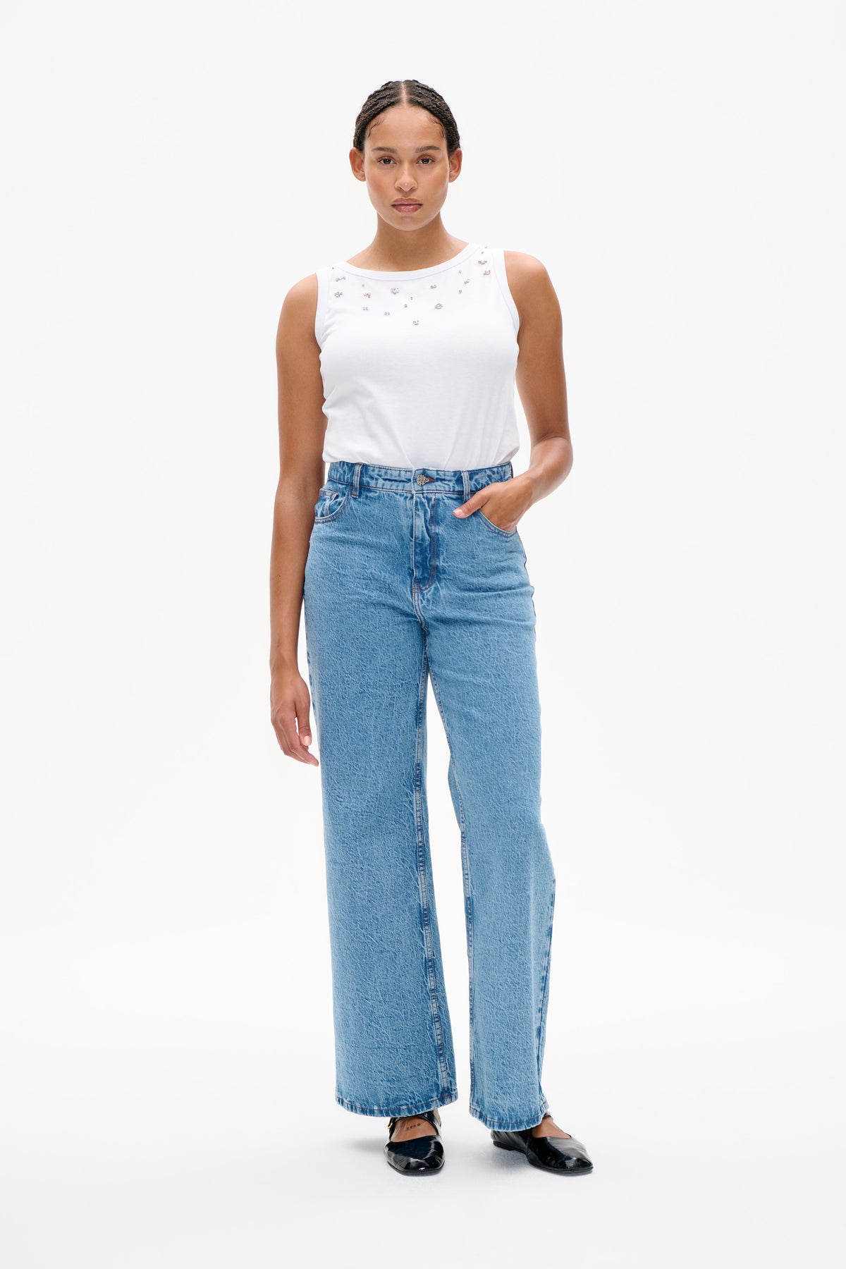 Front view of a white sleeveless top with scattered silver embellishments, styled with light-wash wide-leg jeans.