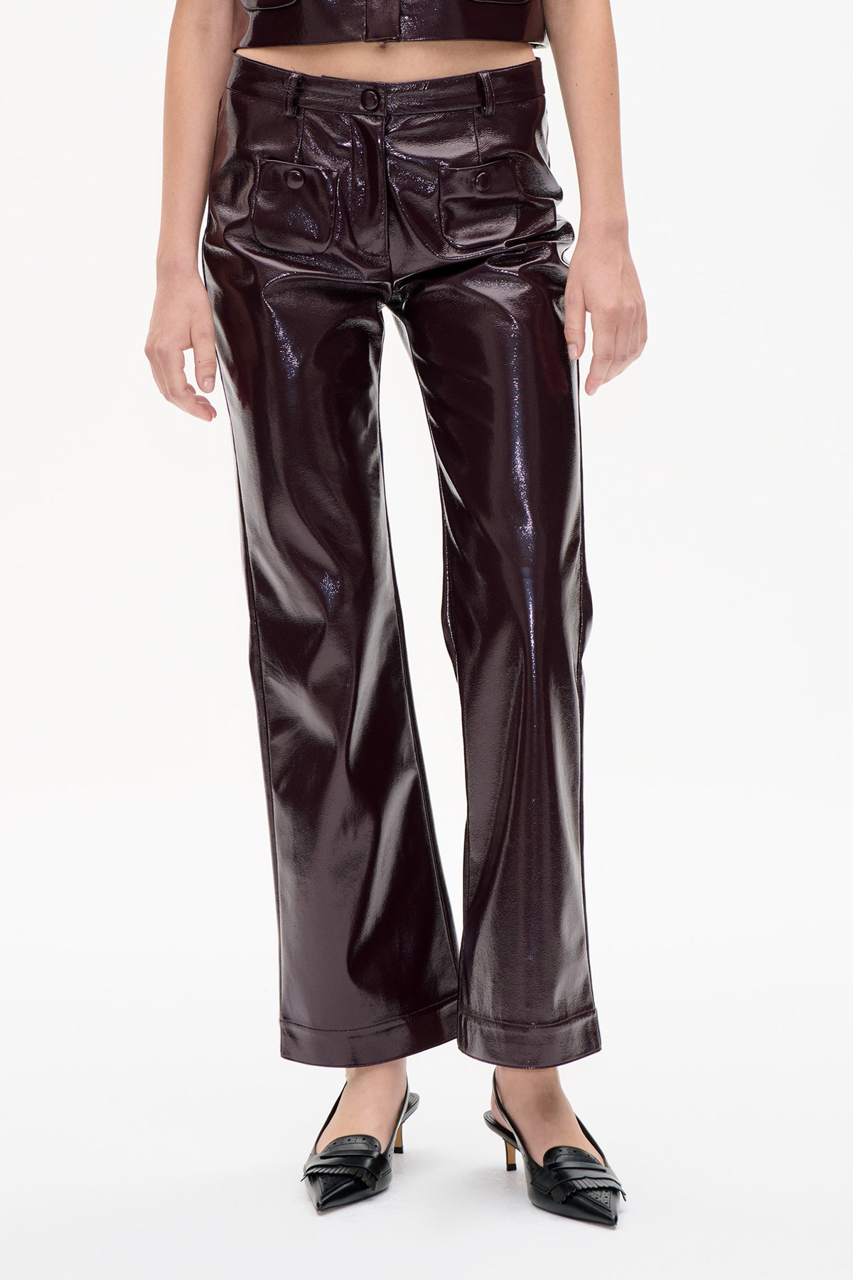Détail avant d'un pantalon à jambes larges en tissu brillant marron foncé, taille boutonnée et poches plaquées oversized, porté avec un top court assorti.
