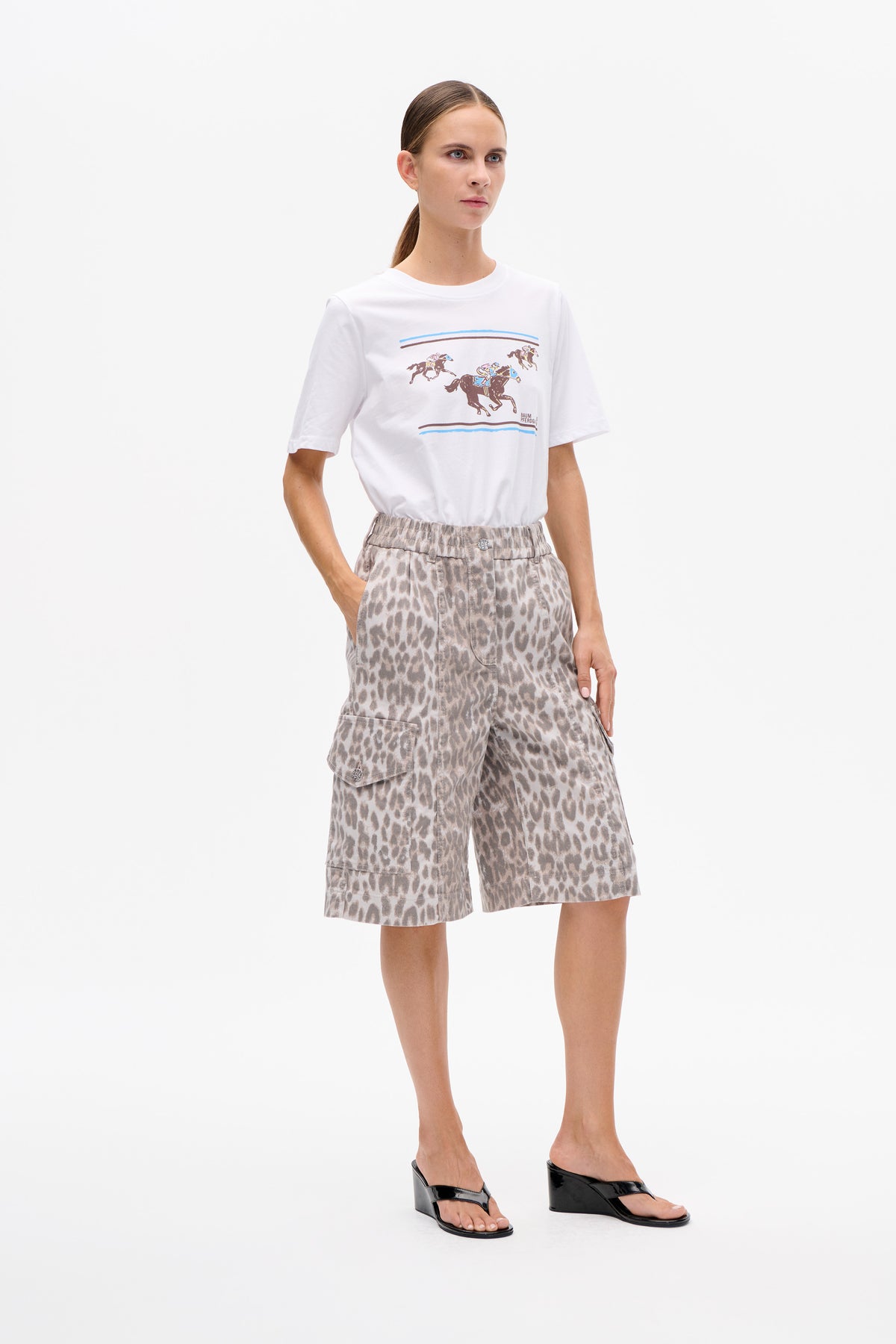 Front view of a white short-sleeved T-shirt with a colourful horse-racing graphic, paired with grey animal-print shorts.
