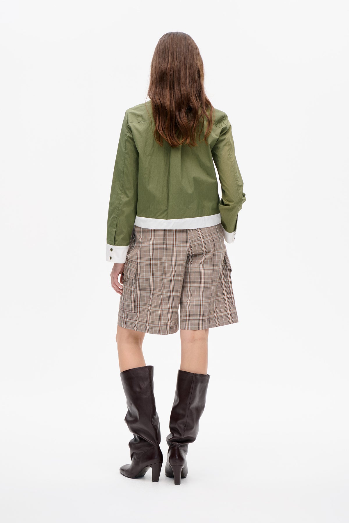 Back view of an olive-green long-sleeved shirt with white hem and cuffs, paired with beige plaid shorts and dark knee-high boots.