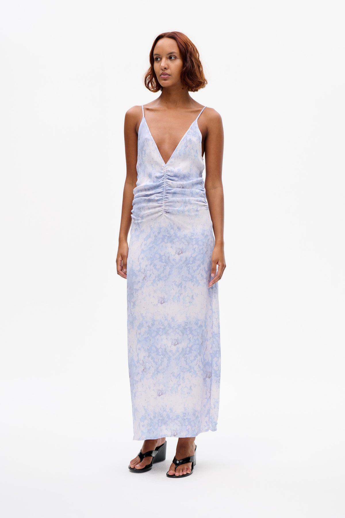 Front view of a pale blue and lavender printed slip dress with thin straps, a deep V neckline and ruched centre.