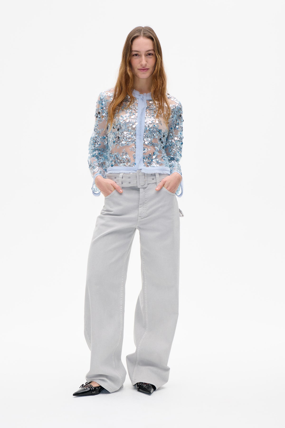 Front view of a model wearing a sheer pale blue blouse covered in silver and blue sequins, with a ruffled neckline and matching trim.