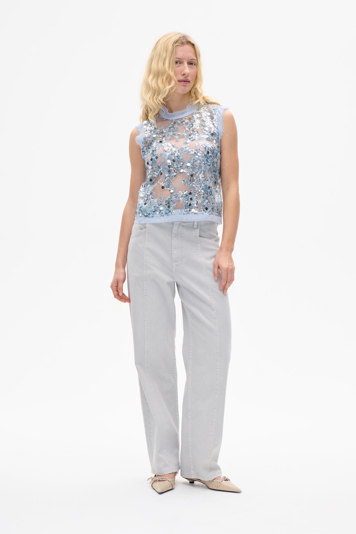 Front view of a pale blue sleeveless sheer top covered in silver and blue sequins, styled with light grey jeans.