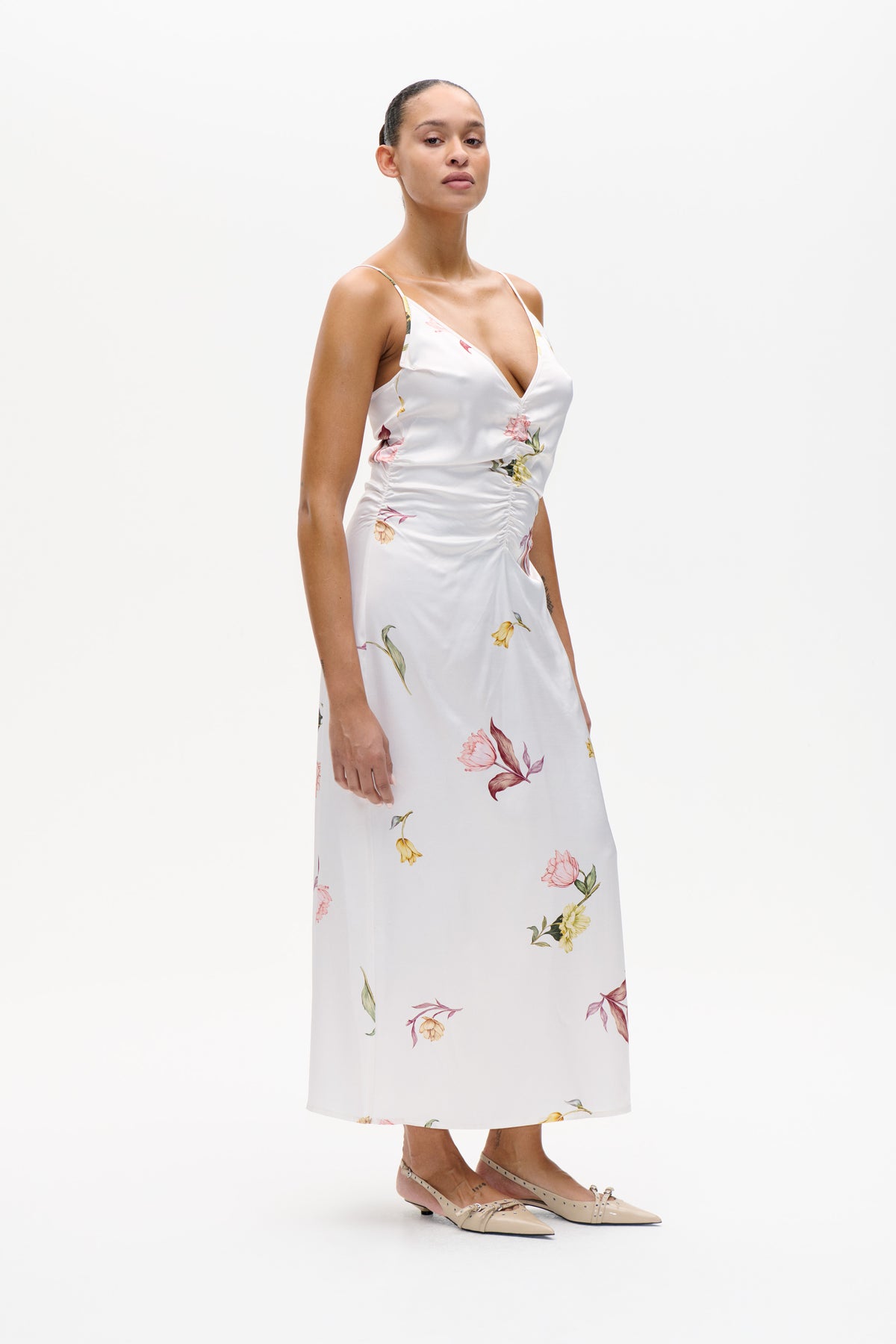 Model wearing a white spaghetti-strap midi dress with a deep V neckline, ruched side seam and scattered multicoloured floral print.