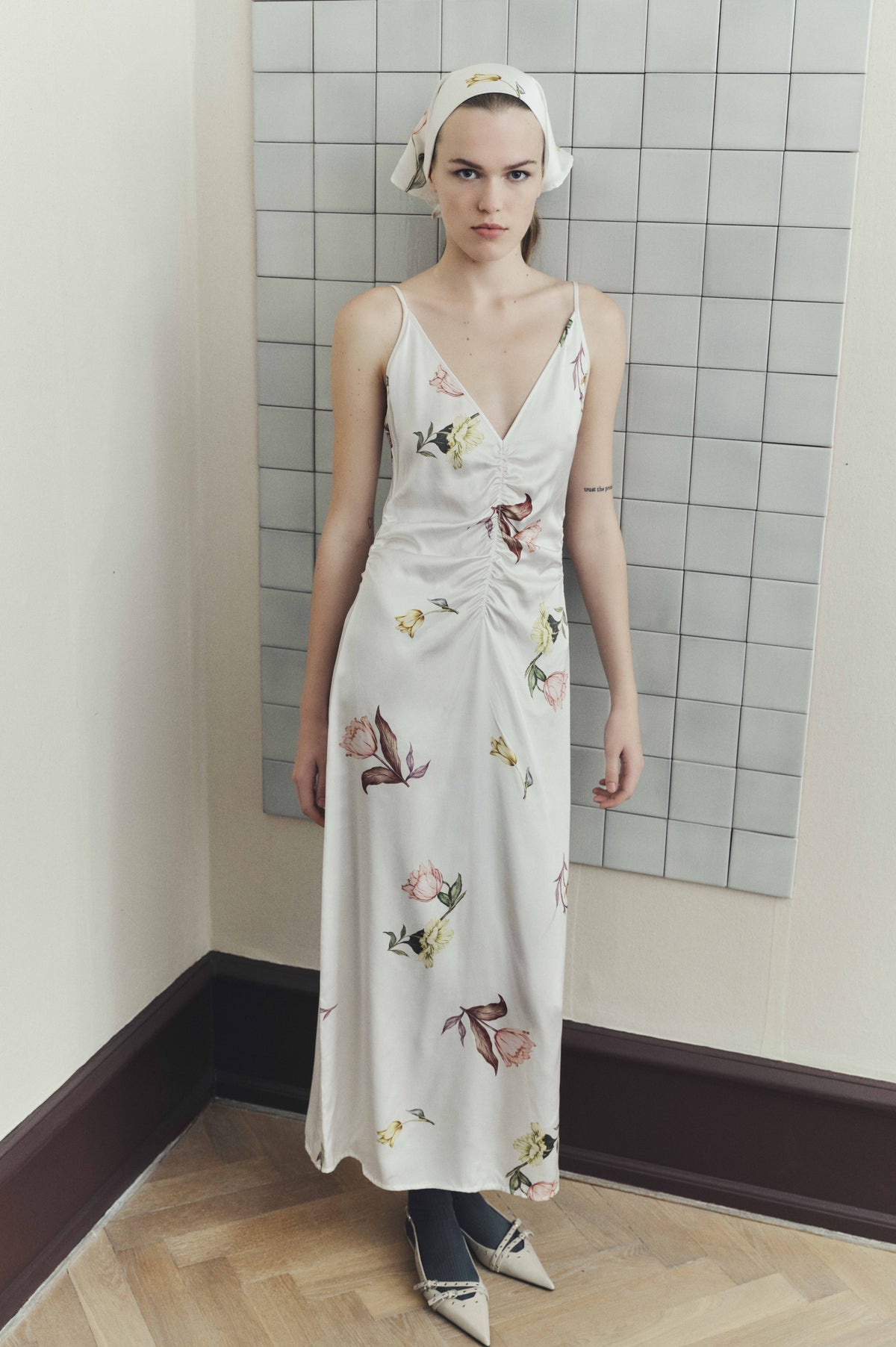 Model wearing a white floral-print slip dress with a deep V-neck and gathered front, styled with a matching headscarf.