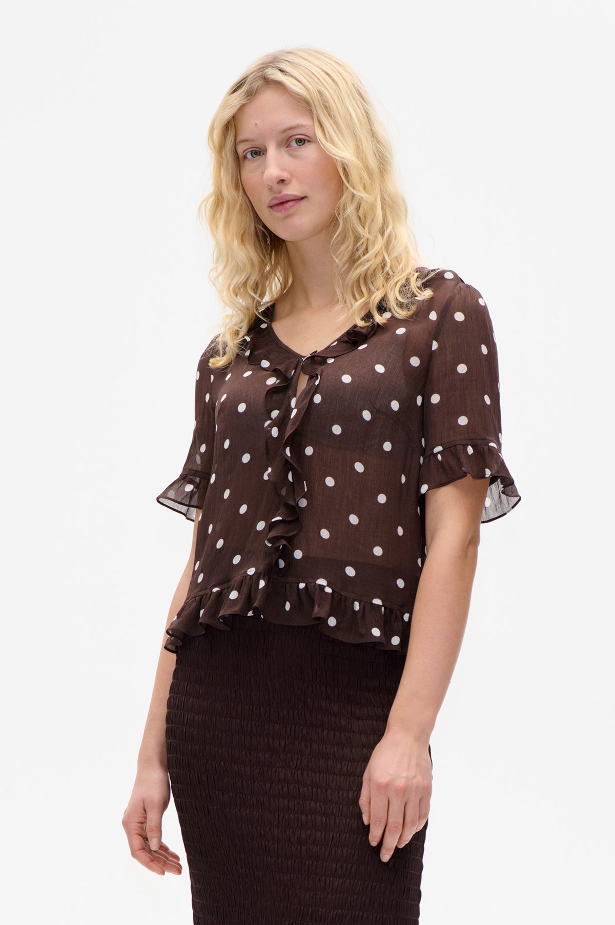 Front view of a dark brown blouse with white polka dots, a ruffled neckline and front, and short flounced sleeves.