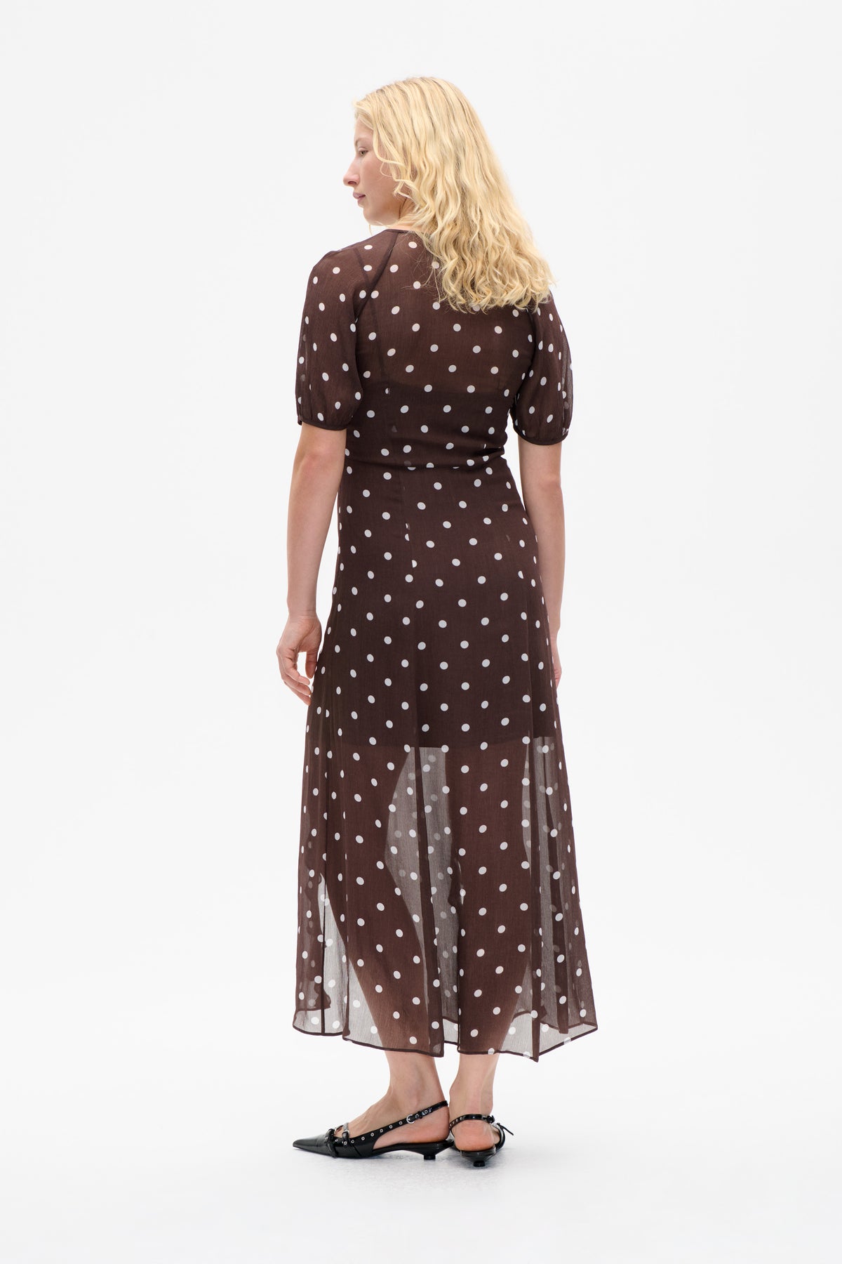 Back view of a sheer dark brown midi dress with white polka dots and short puff sleeves.