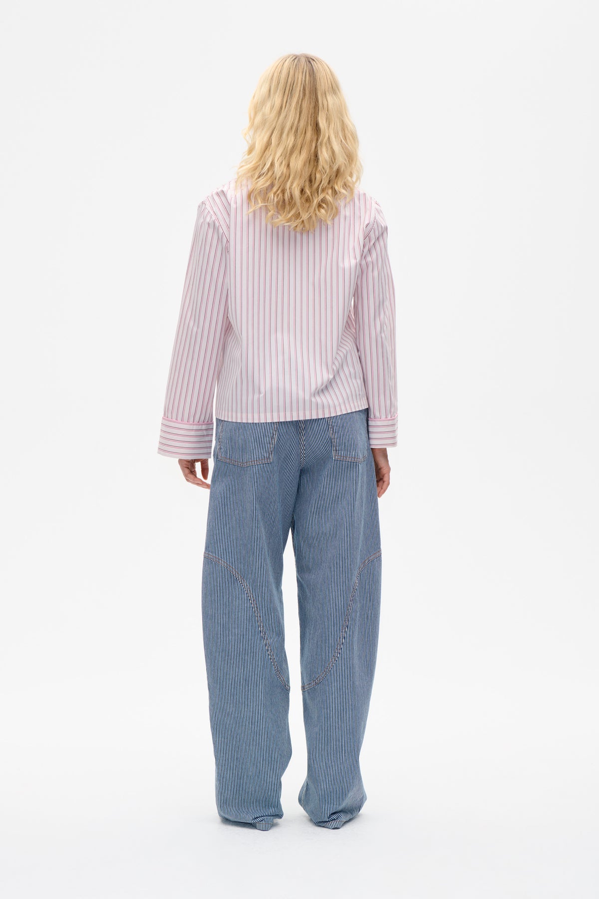 Back view of a white shirt with thin pink vertical stripes and wide cuffs, paired with blue pinstriped wide-leg trousers.