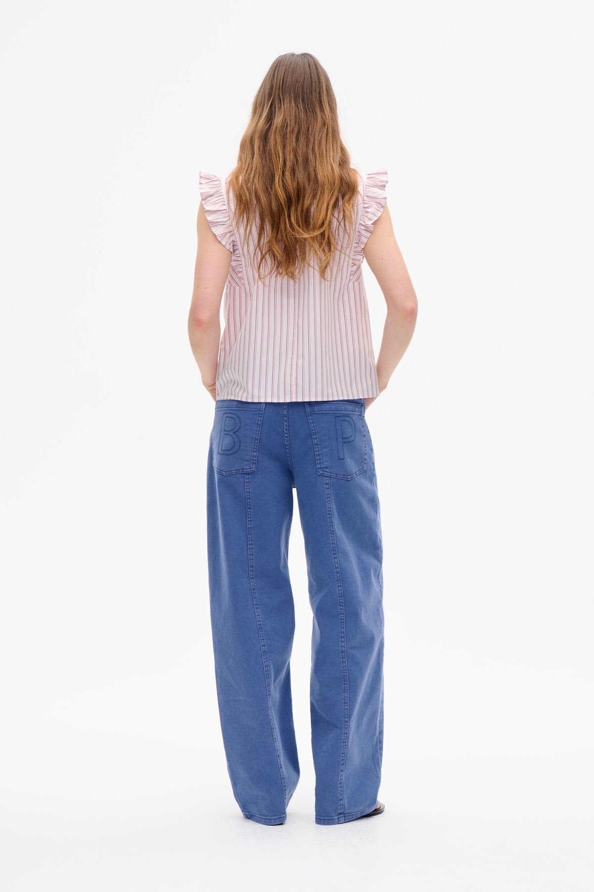 Achteraanzicht van een wit mouwloos topje met fijne roze verticale strepen en ruches op de schouders, gedragen met wijde blauwe jeans.