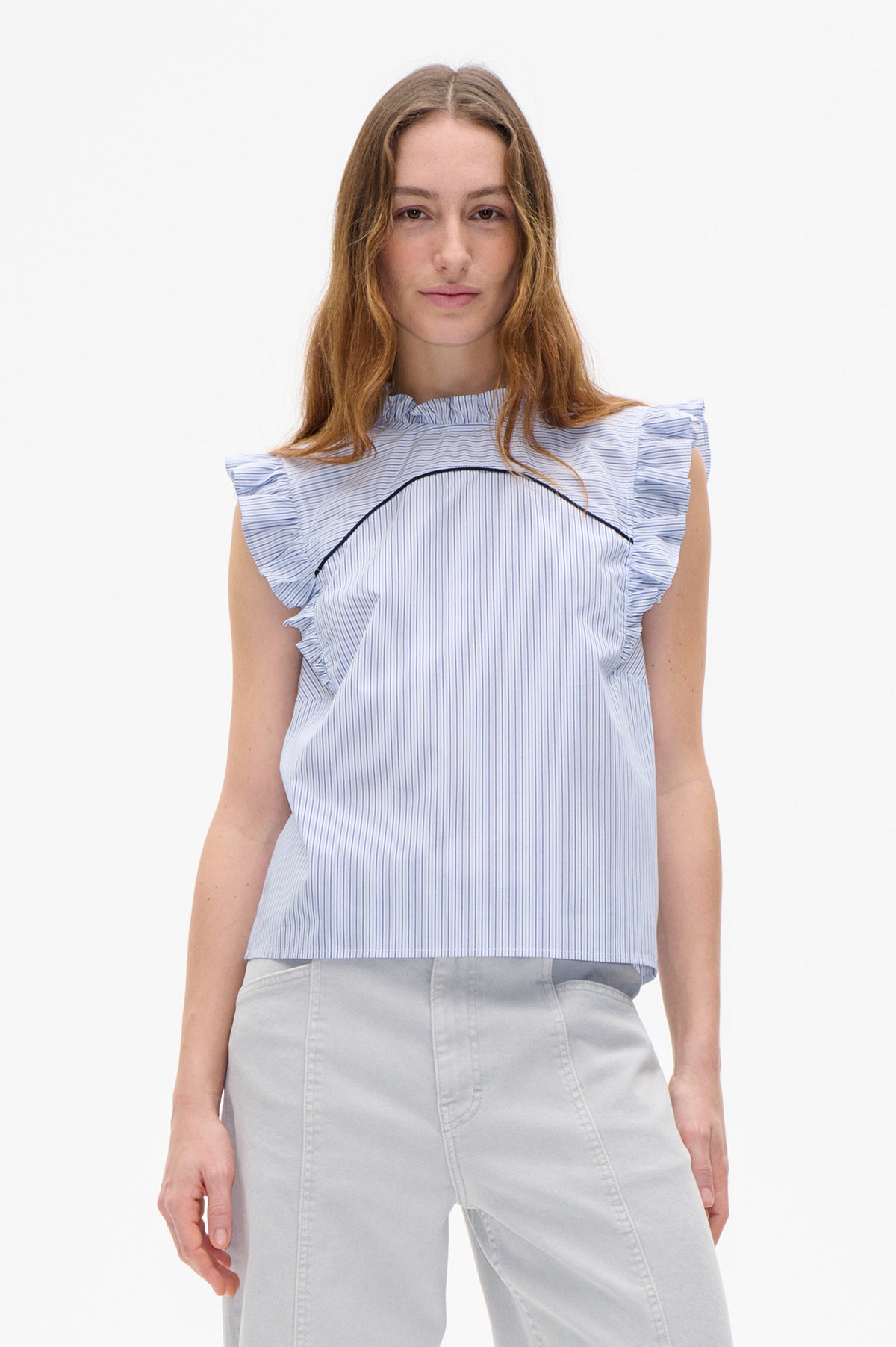 Vooraanzicht van een witte blouse met fijne blauwe strepen, ruches op de schouders en een gebogen zwarte bies, gecombineerd met een lichtgrijze broek.