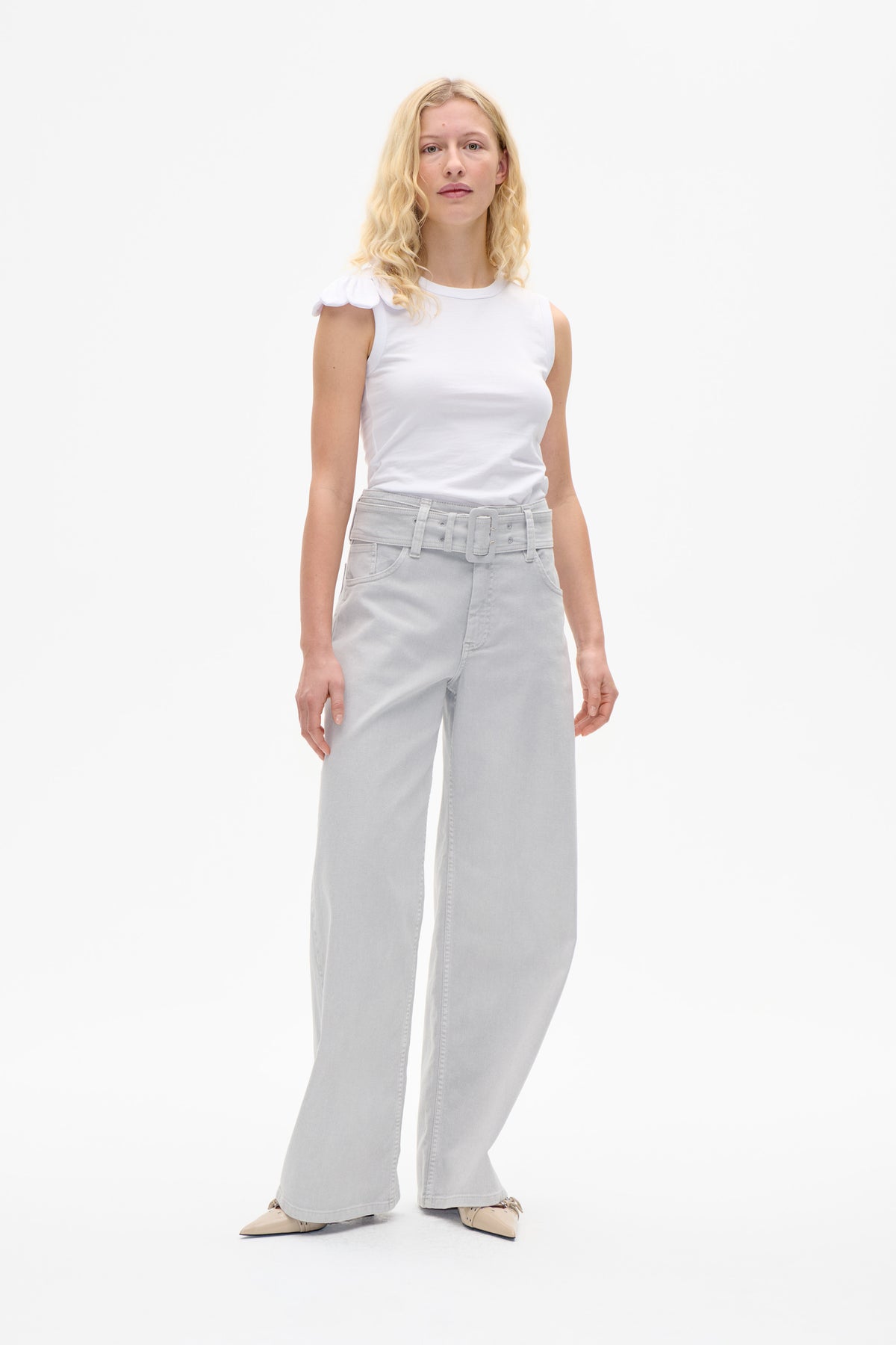 Model wearing a white sleeveless top with petal-shaped shoulder trim and pale grey wide-leg jeans with a matching belt.