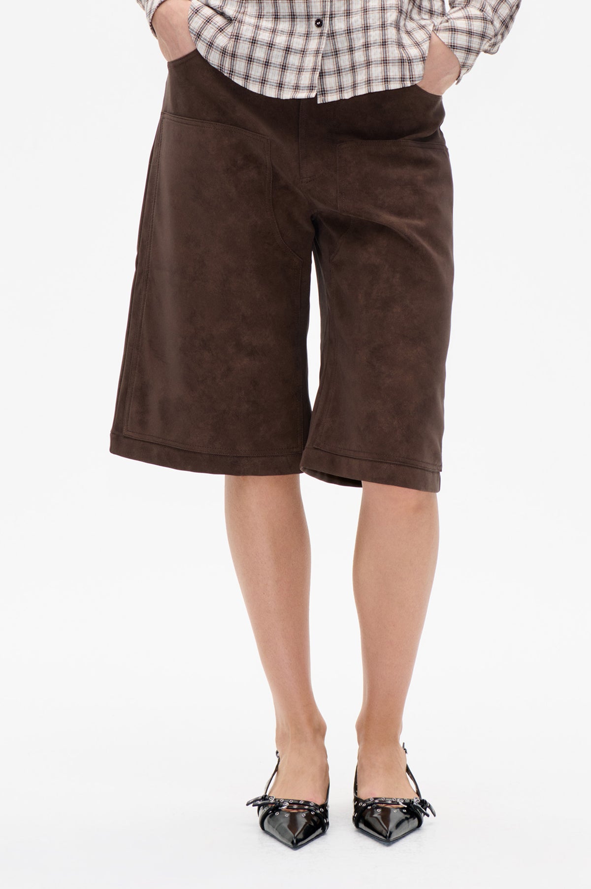 Front detail of dark brown knee-length shorts with wide legs and large patch pockets, paired with a light plaid shirt.