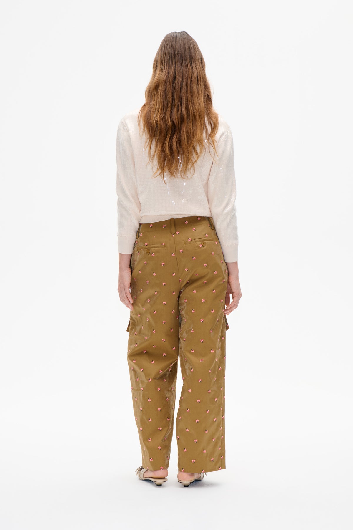 Rückenansicht eines Models, das ein elfenbeinfarbenes Langarmtop mit vereinzelten Pailletten und eine ockerfarbene, mit kleinen rosa Blumen bedruckte Hose trägt.