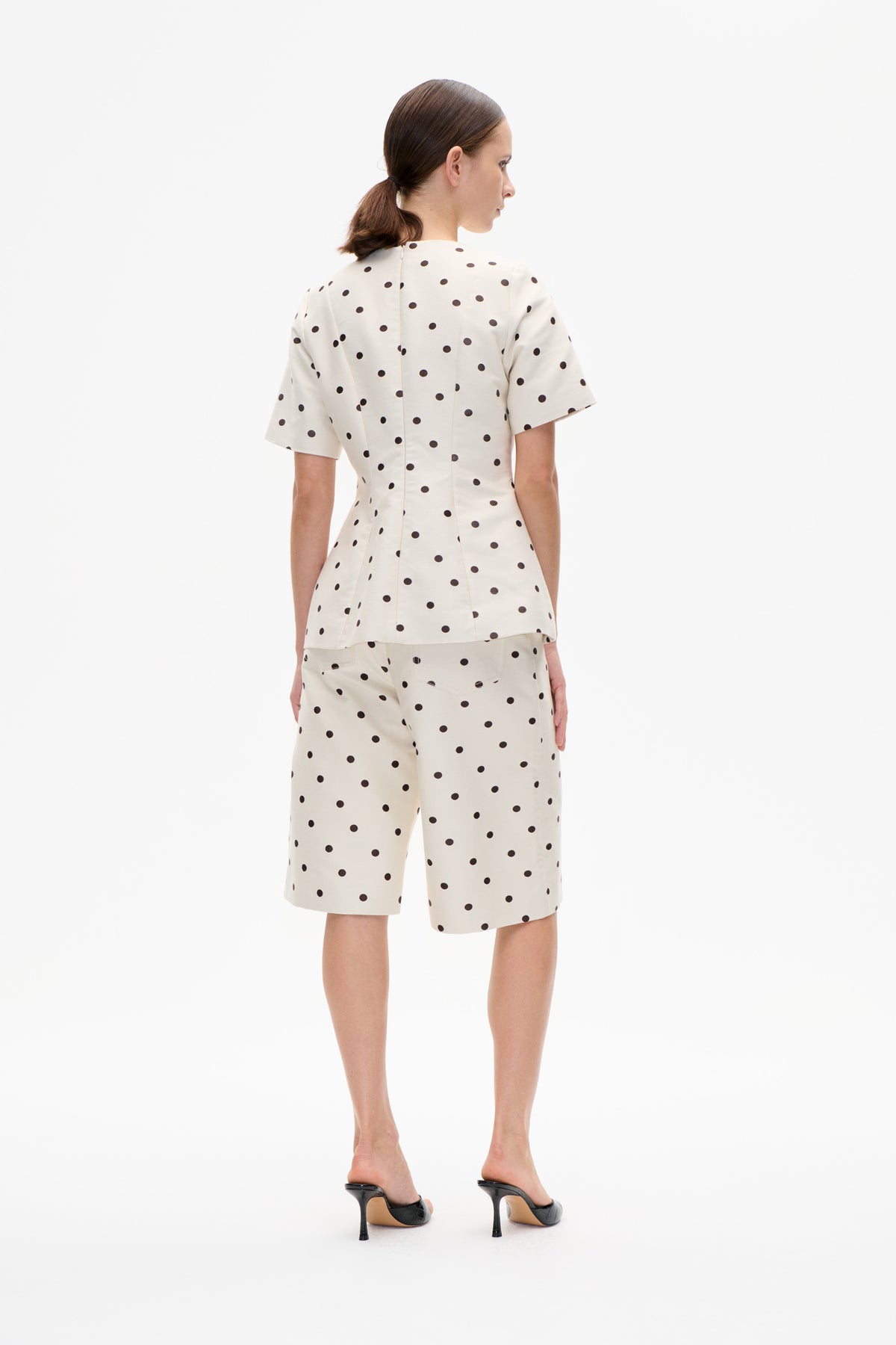 Back view of a model wearing a cream short-sleeved top and matching knee-length shorts with black polka dots.