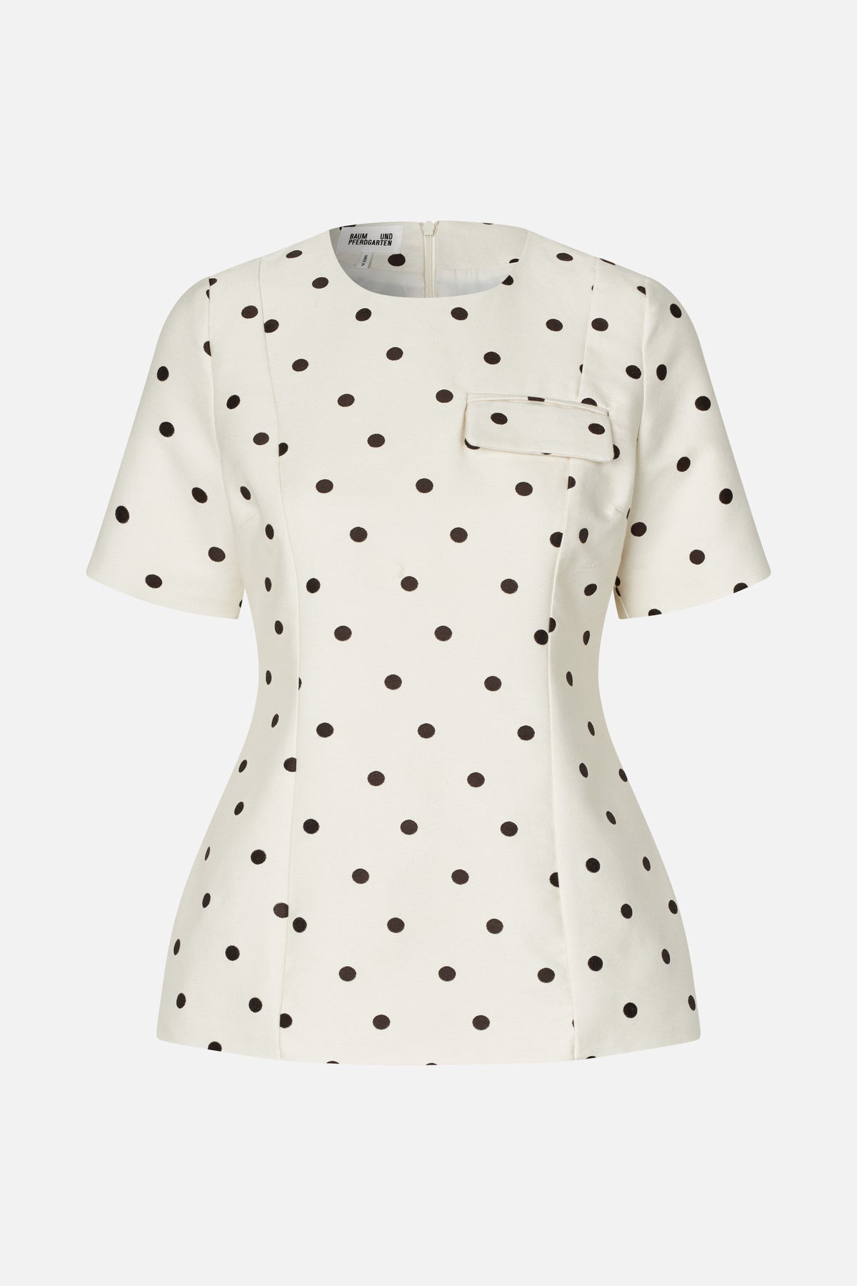 Ivory short-sleeved top with dark polka dots, a rounded neckline and flap chest pocket, shown from the front.