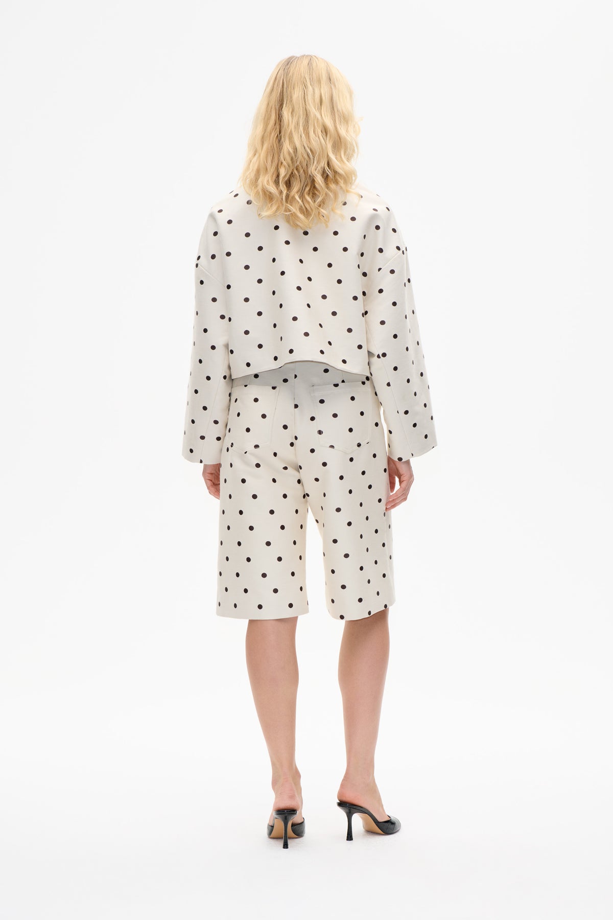 Back view of a model wearing a cream long-sleeved top and knee-length shorts with black polka dots.