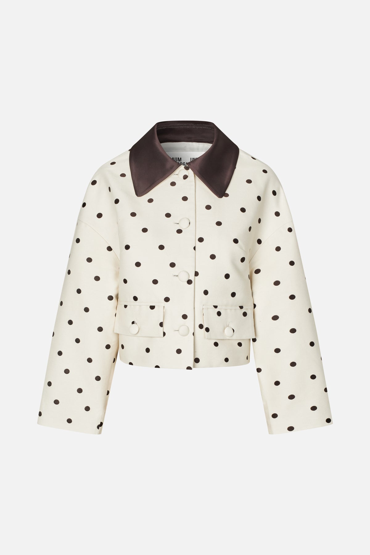 Front view of a cropped cream jacket with dark brown polka dots, a wide contrasting collar, button fastening and flap pockets.