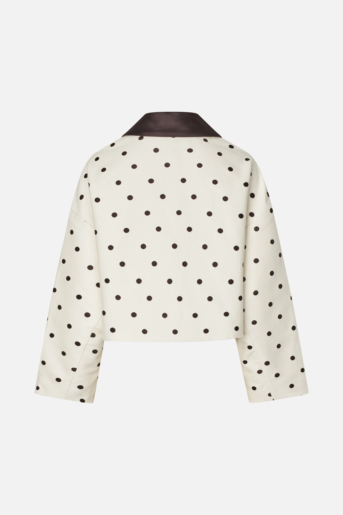 Back view of a cream cropped jacket with dark brown polka dots, long sleeves, and a contrasting brown collar.