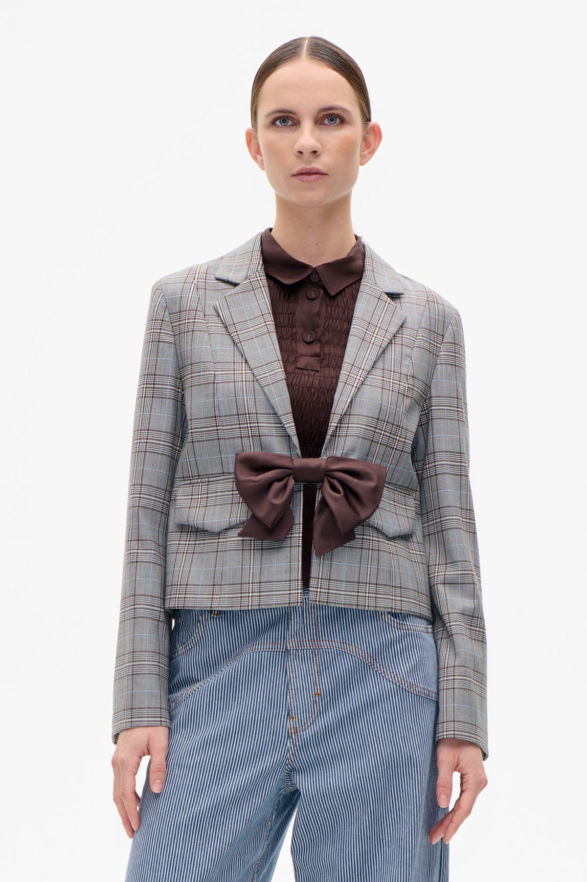 Front view of a model wearing a grey plaid blazer over a dark brown quilted shirt and blue-and-white pinstriped trousers.